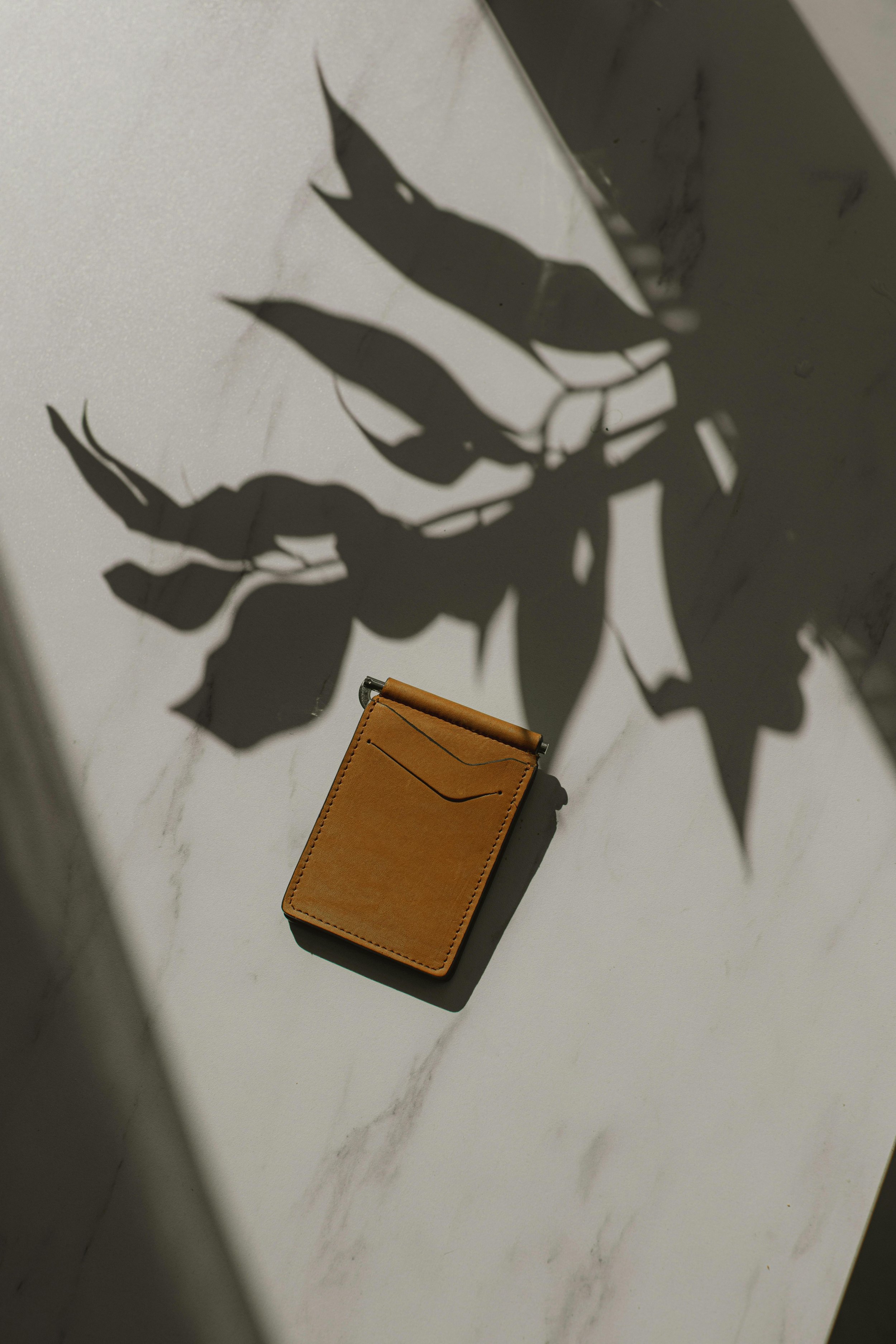 A leather wallet with a shadow cast by a plant on a white marble surface.