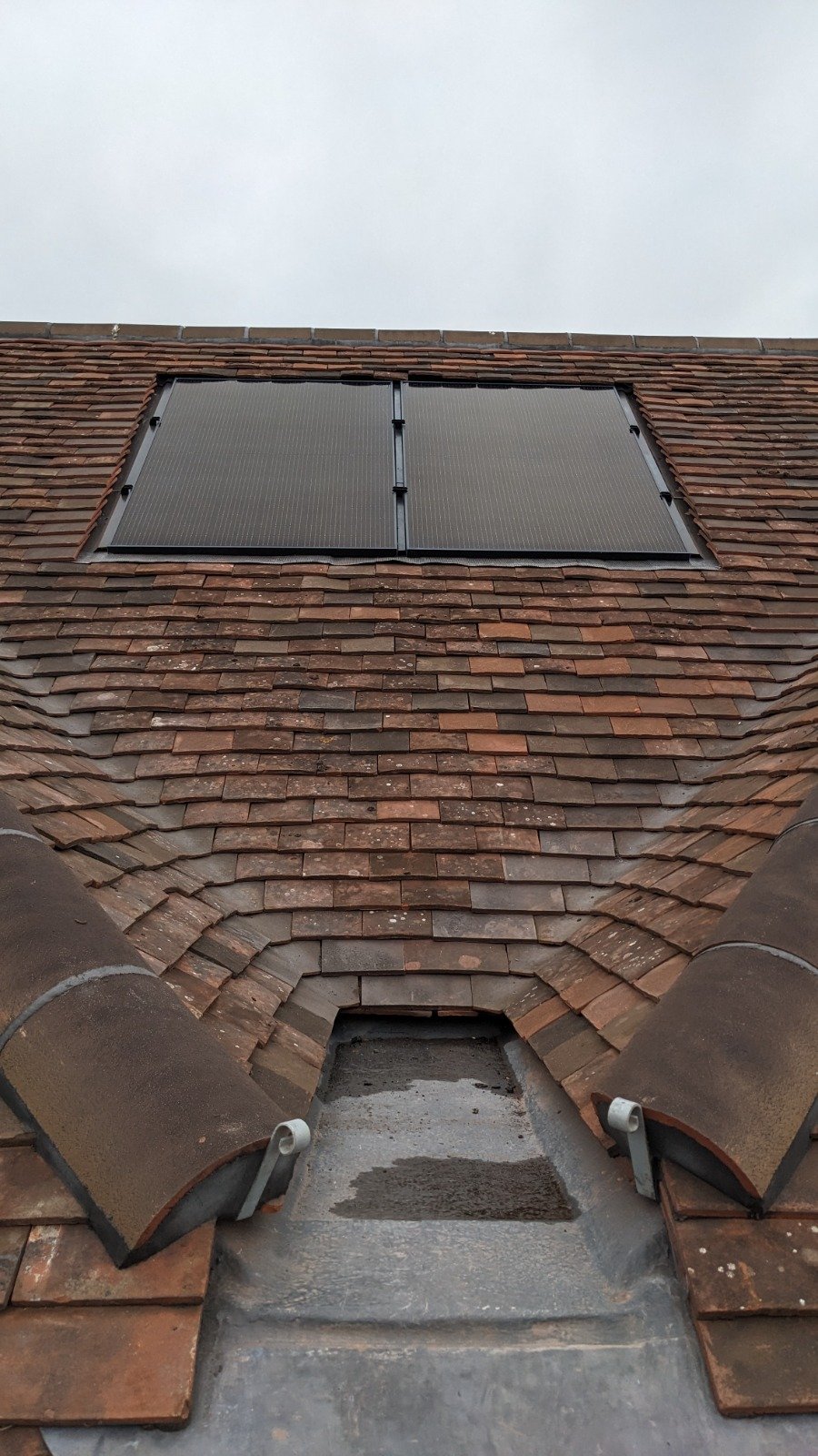 A rooftop with red clay tiles and a solar panel installed in the center, viewed from lower on the roof.