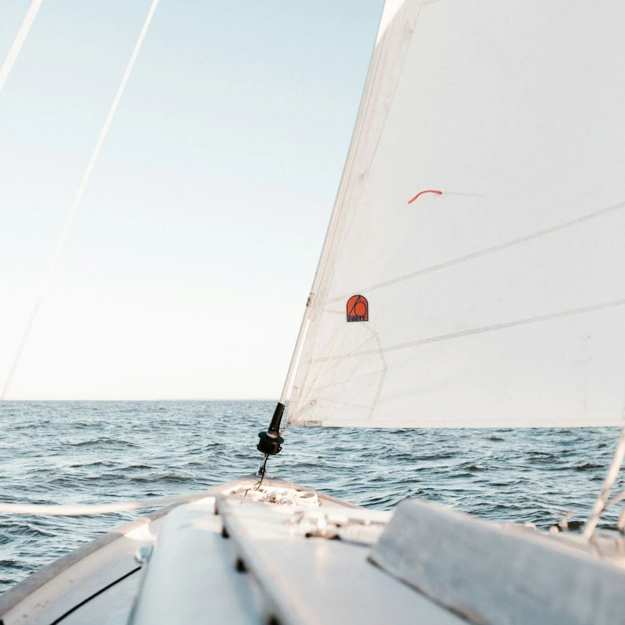 Photo from the deck of a sailing boat showing the ocean water and the sail.