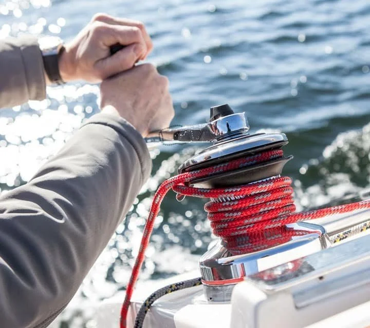 Close-up of a person adjusting the winch with a red rope on a boat in the water.