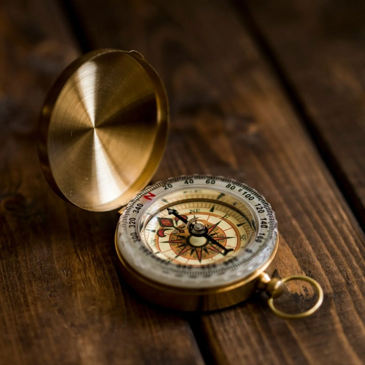A vintage gold-colored compass with its lid open, resting on a wooden surface.