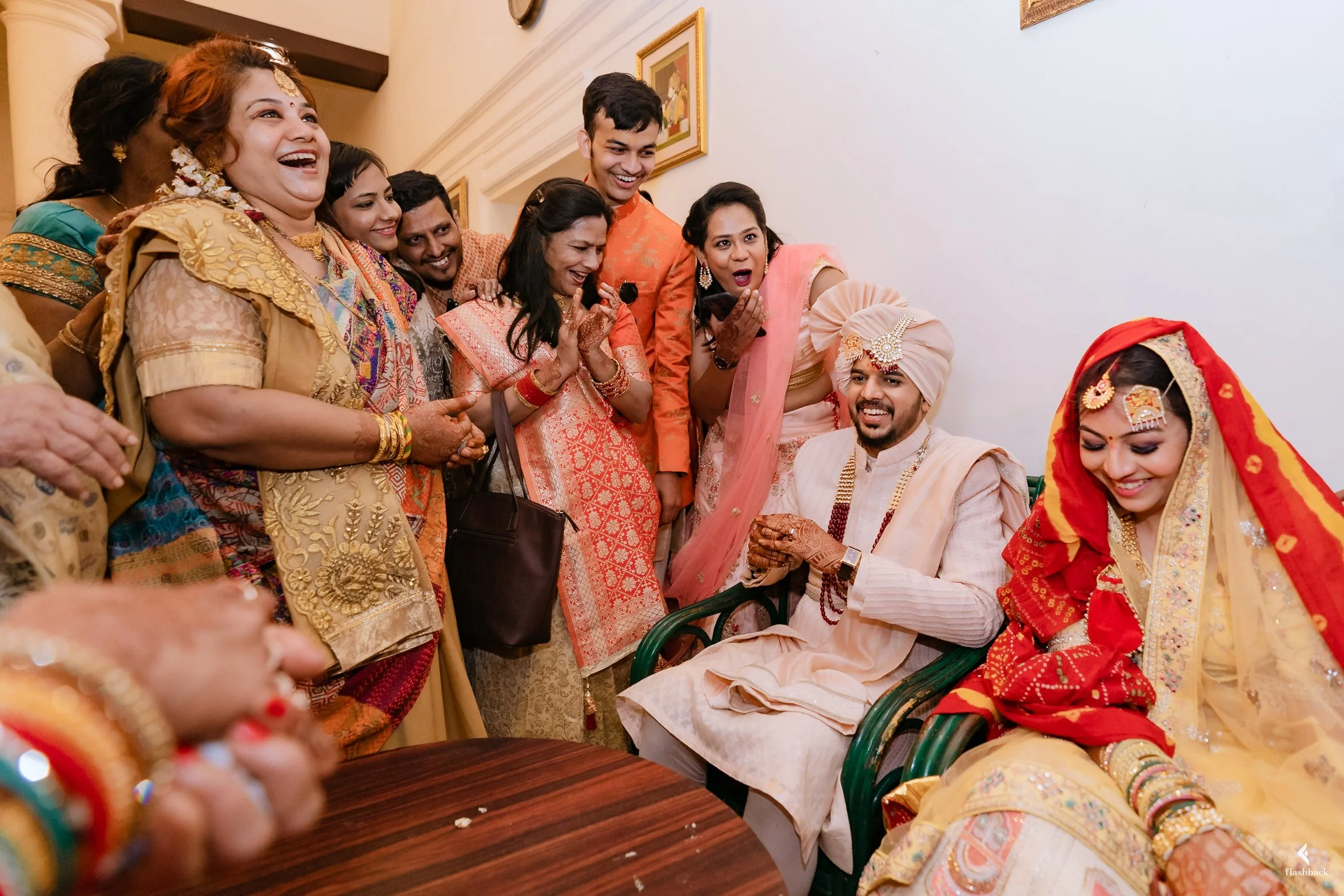 A group of people in traditional Indian attire gathered around a seated bride and groom, celebrating at a wedding.