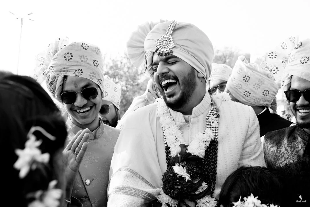 A group of people celebrating a traditional Indian wedding, with men wearing turbans and smiling, one of whom is singing or shouting joyfully.