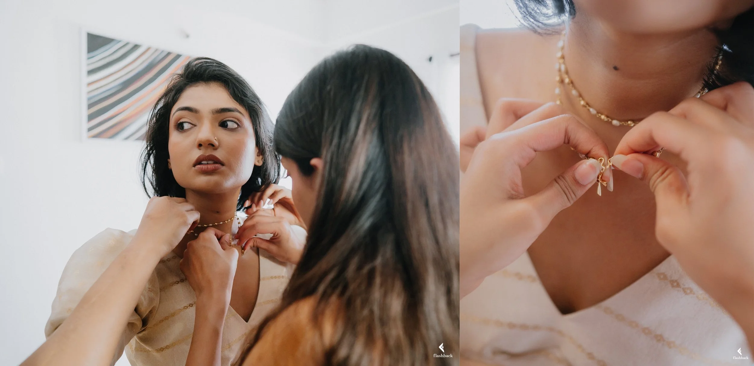 Two women are putting on gold jewelry, one woman is helping the other with her necklace, while the woman receiving the jewelry looks into the mirror, wearing a cream-colored top with a delicate gold chain, a small nose ring, and a pearl necklace.