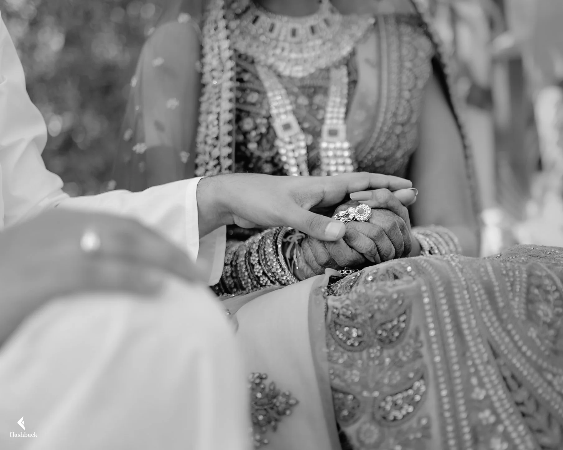 Close-up of a groom holding the bride's hand during a wedding ceremony, highlighting their rings, with the bride dressed in traditional, ornate jewelry and attire.
