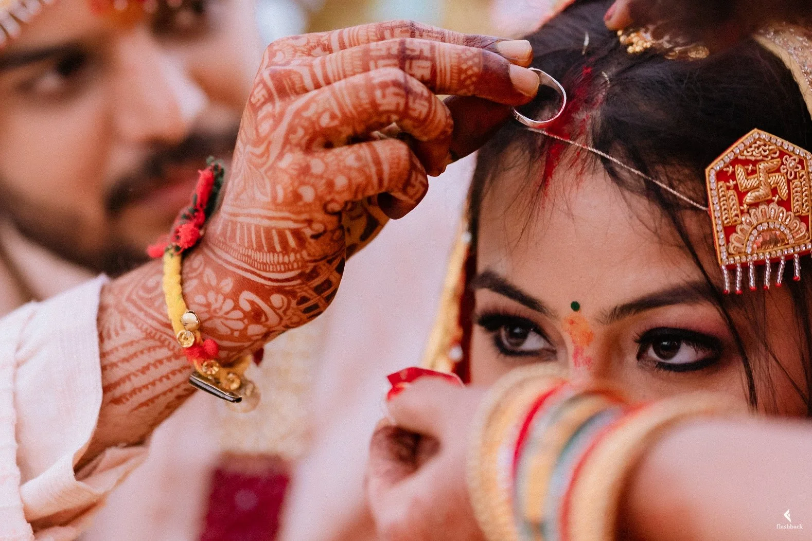 A woman having a traditional Indian wedding tattooing or marking of her forehead with a red powder during a Hindu ritual, observed by an older person.