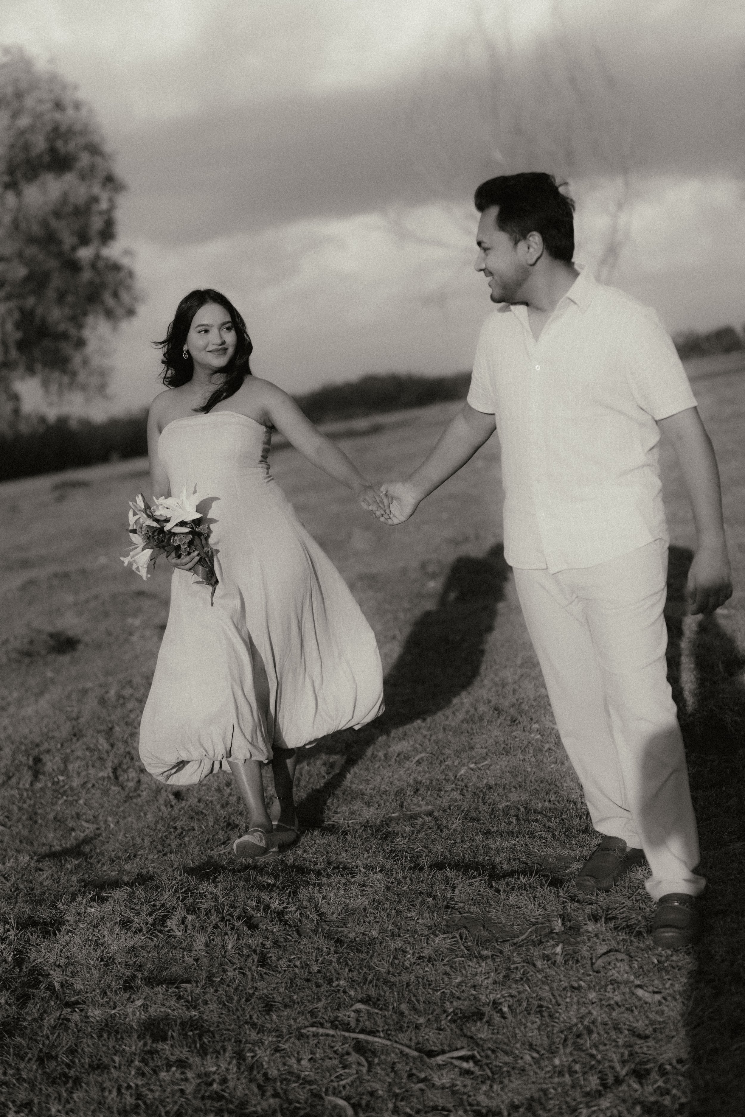 Black and white portrait of a couple holding hands, walking through a field