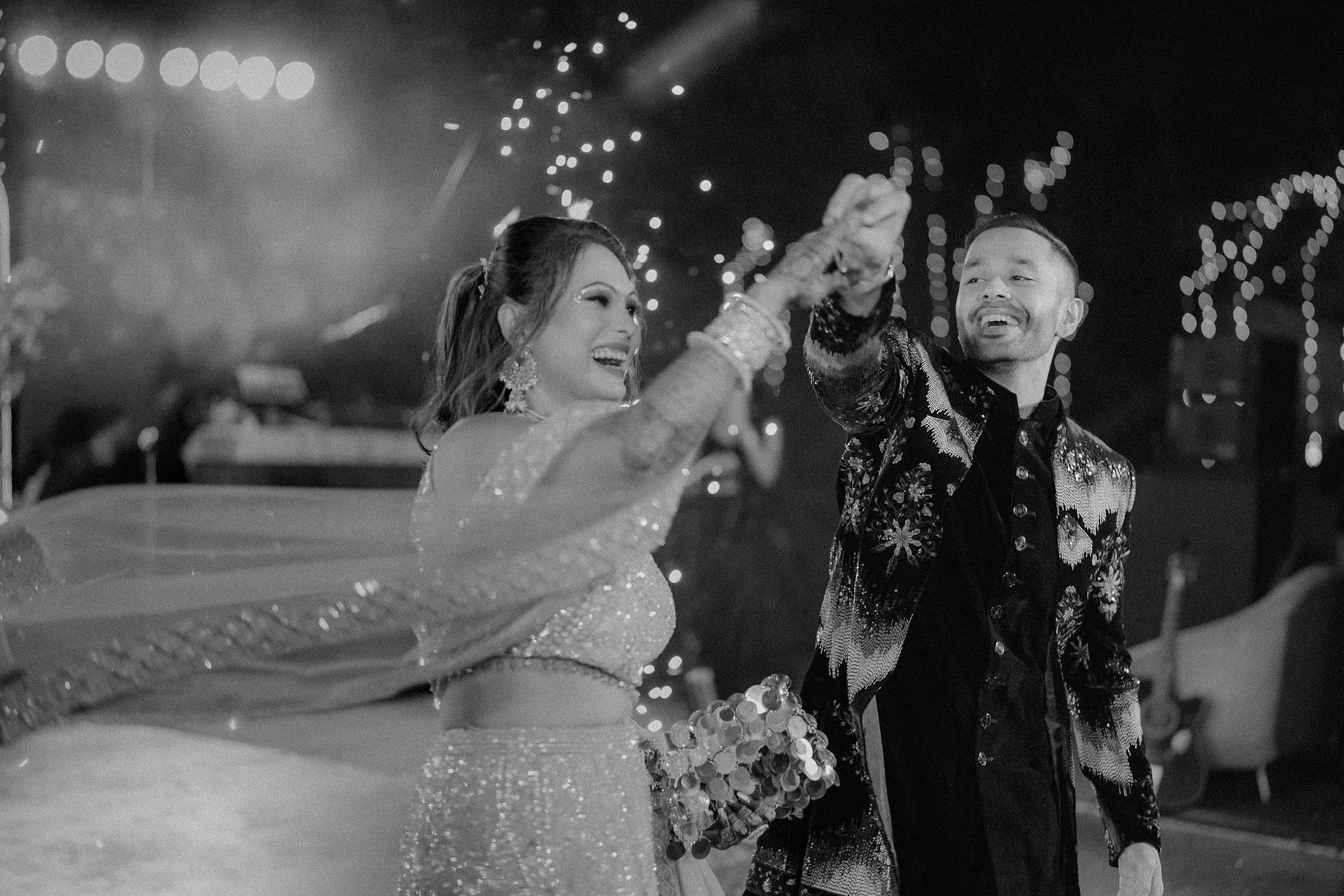 A bride and groom dancing at their wedding reception with smiling faces, holding hands, with string lights in the background.