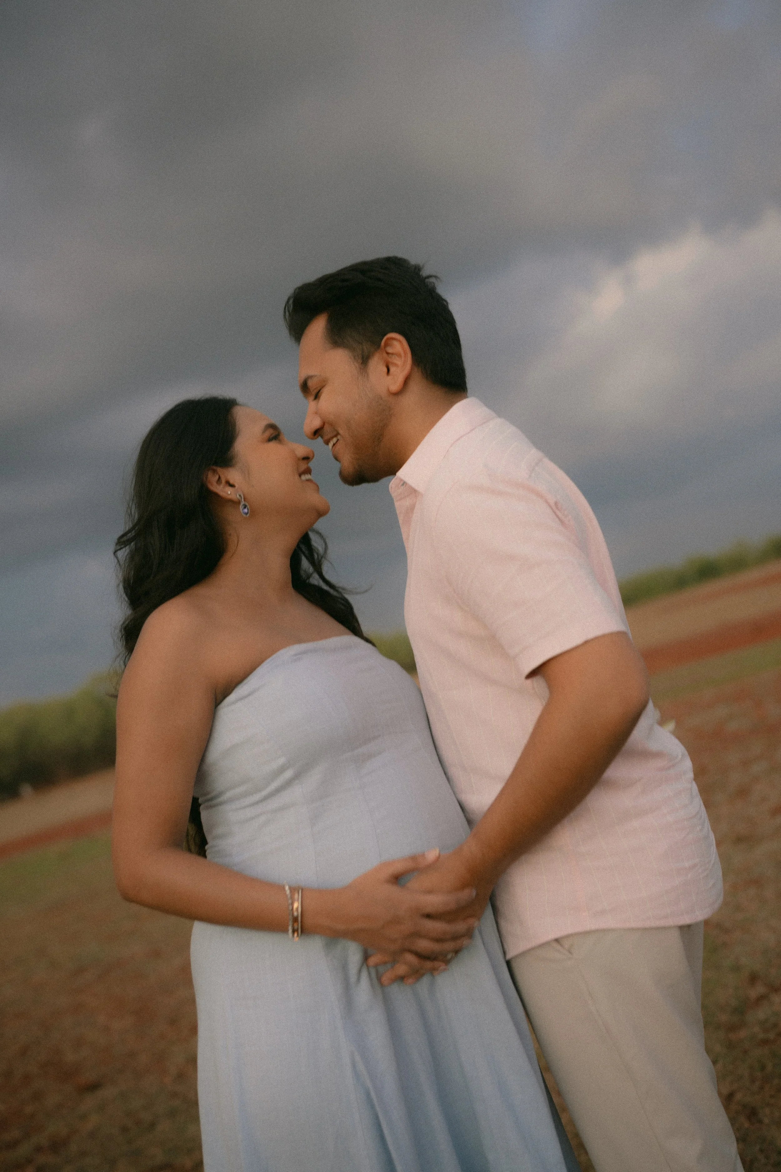 Couple nose to nose, laughing, in front of a stormy sky