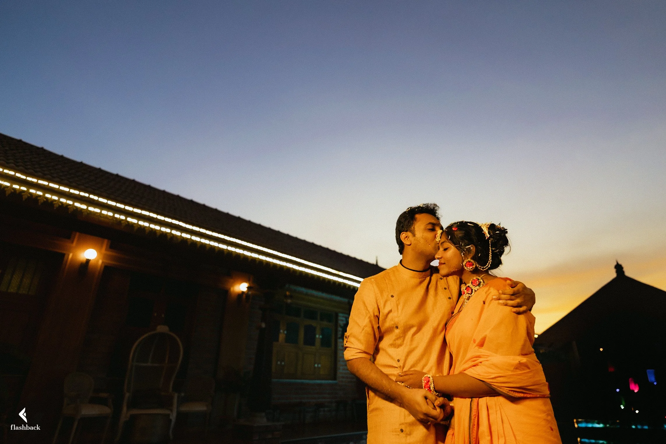 A couple dressed in traditional Indian attire sharing an intimate moment at sunset.