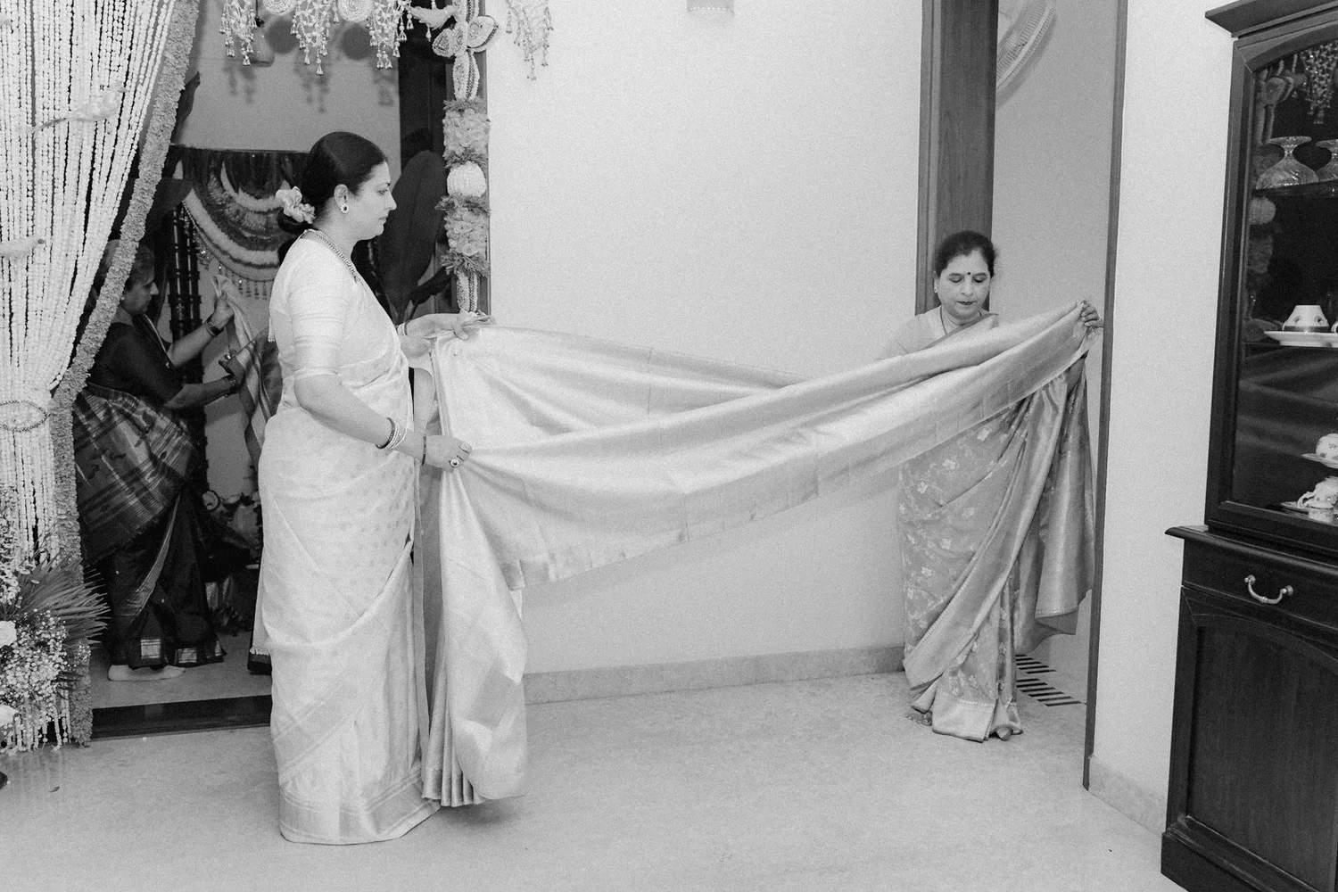 Family members stretching out a silk saree at home, black and white