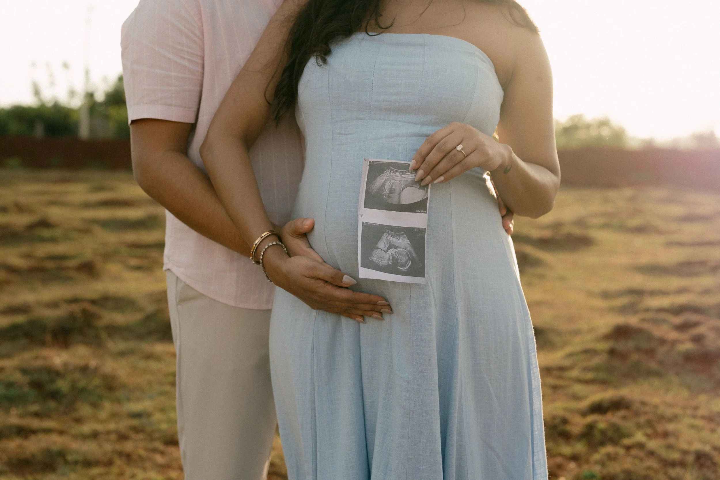 Close detail of hands resting on a baby bump holding ultrasound photos