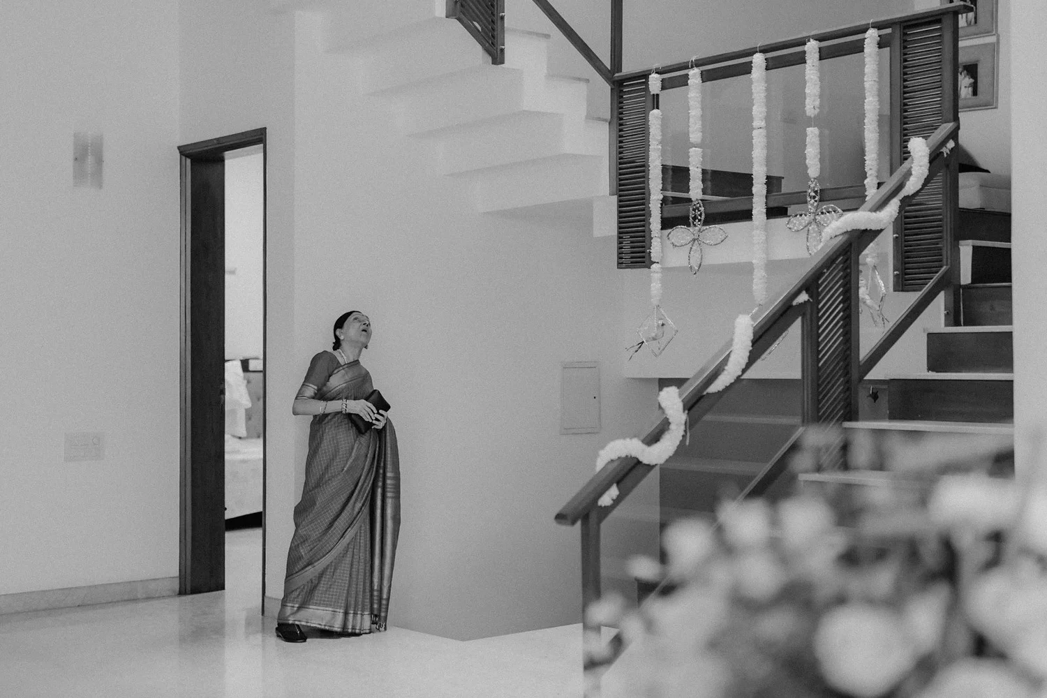 Shrishti's mother waiting at the foot of the stairs, black and white