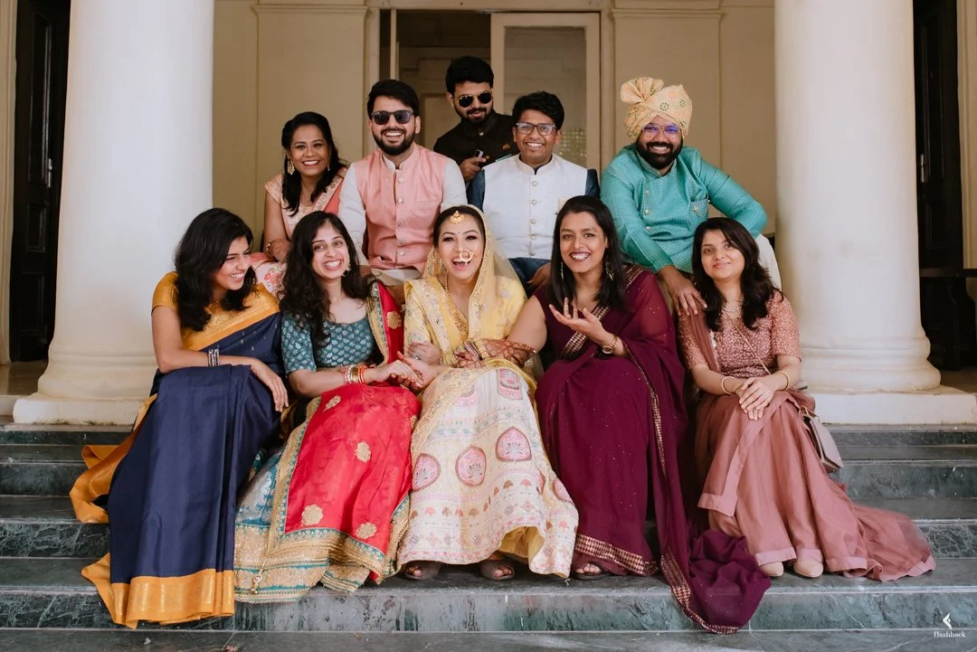A group of ten people dressed in traditional Indian attire posing on steps in front of a building with columns.