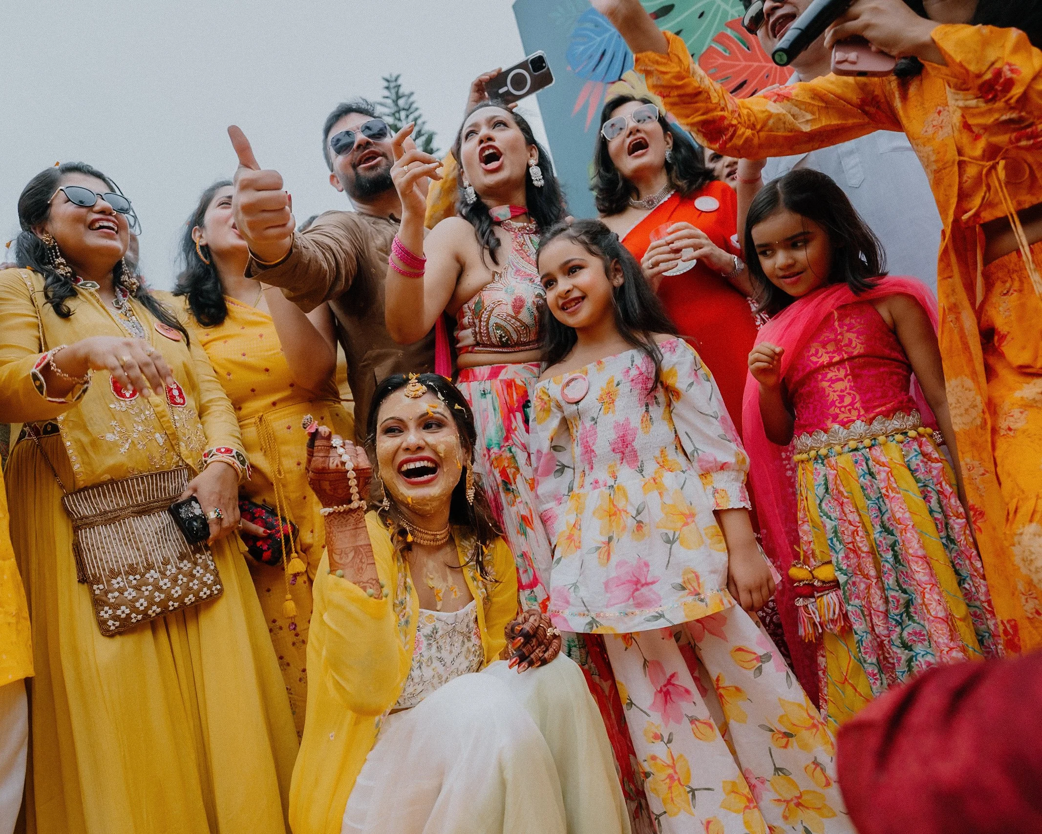 People wearing colorful traditional Indian attire celebrating at an outdoor event, some taking photos and smiling.