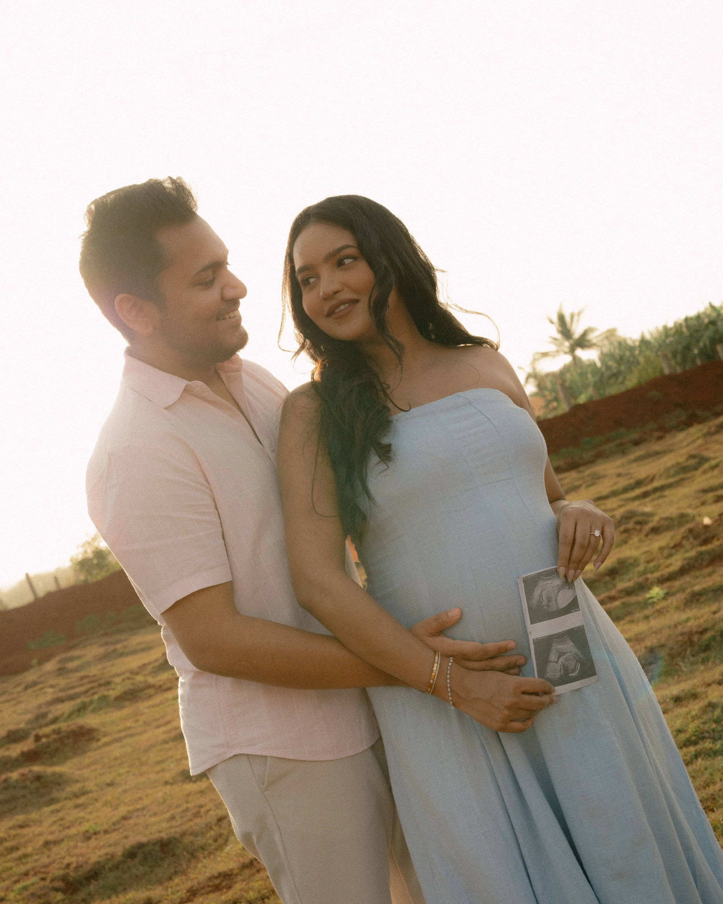 Couple smiling at each other in golden light, holding ultrasound photos