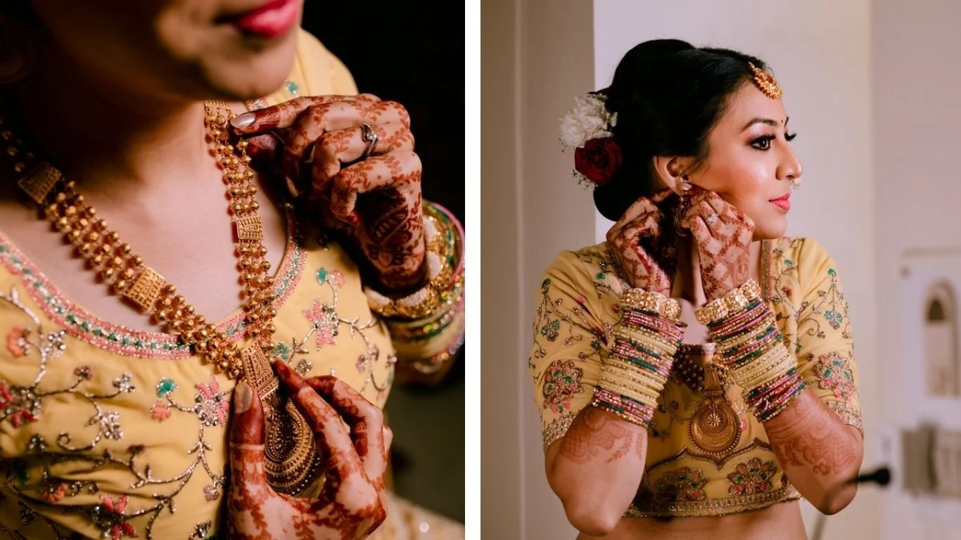 A bride dressed in yellow embroidery, wearing multiple colorful bangles, necklaces, and jewelry, adjusting her earring while showing intricate henna designs on her hands.