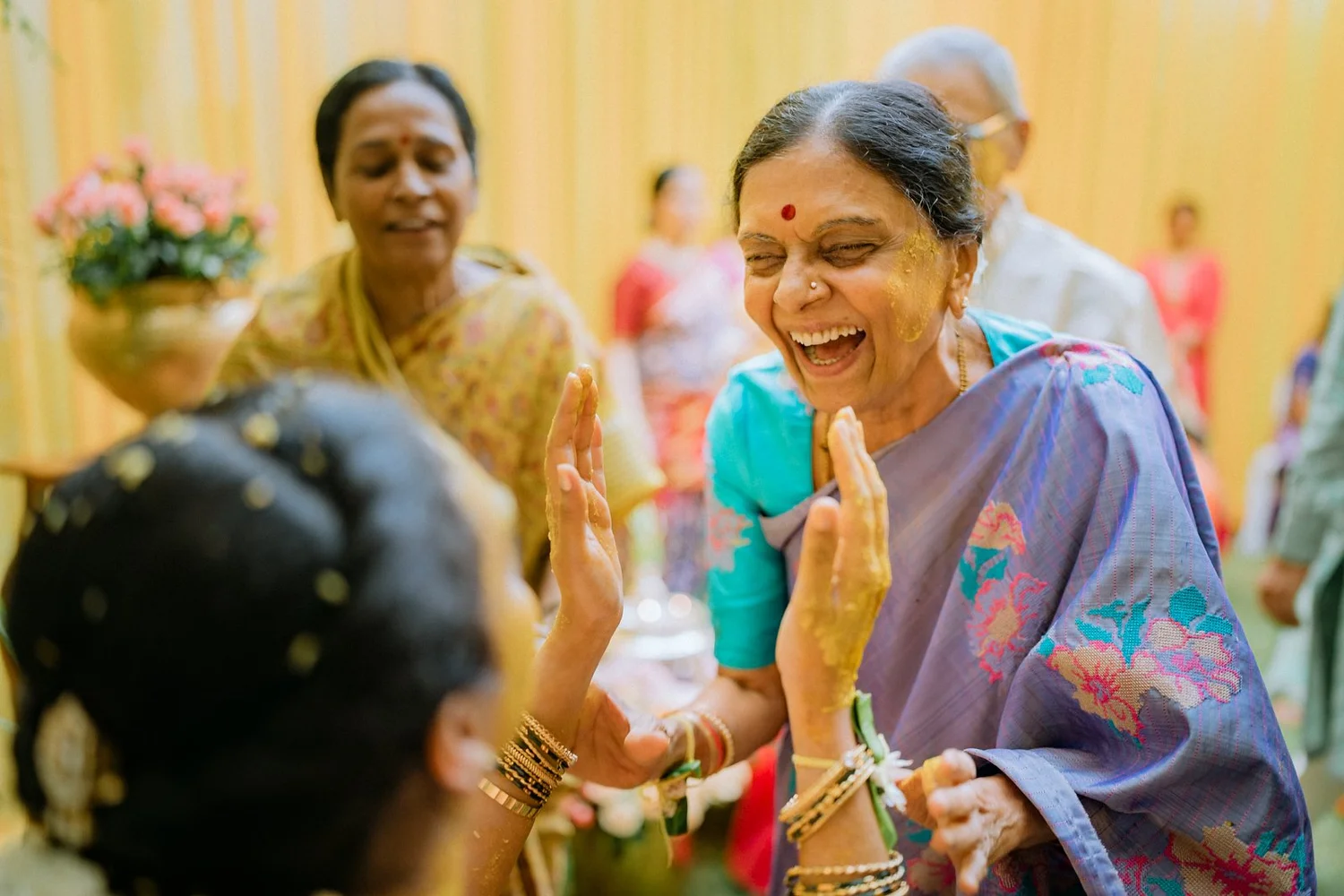 Grandmother laughing as she applies haldi to Shrishti