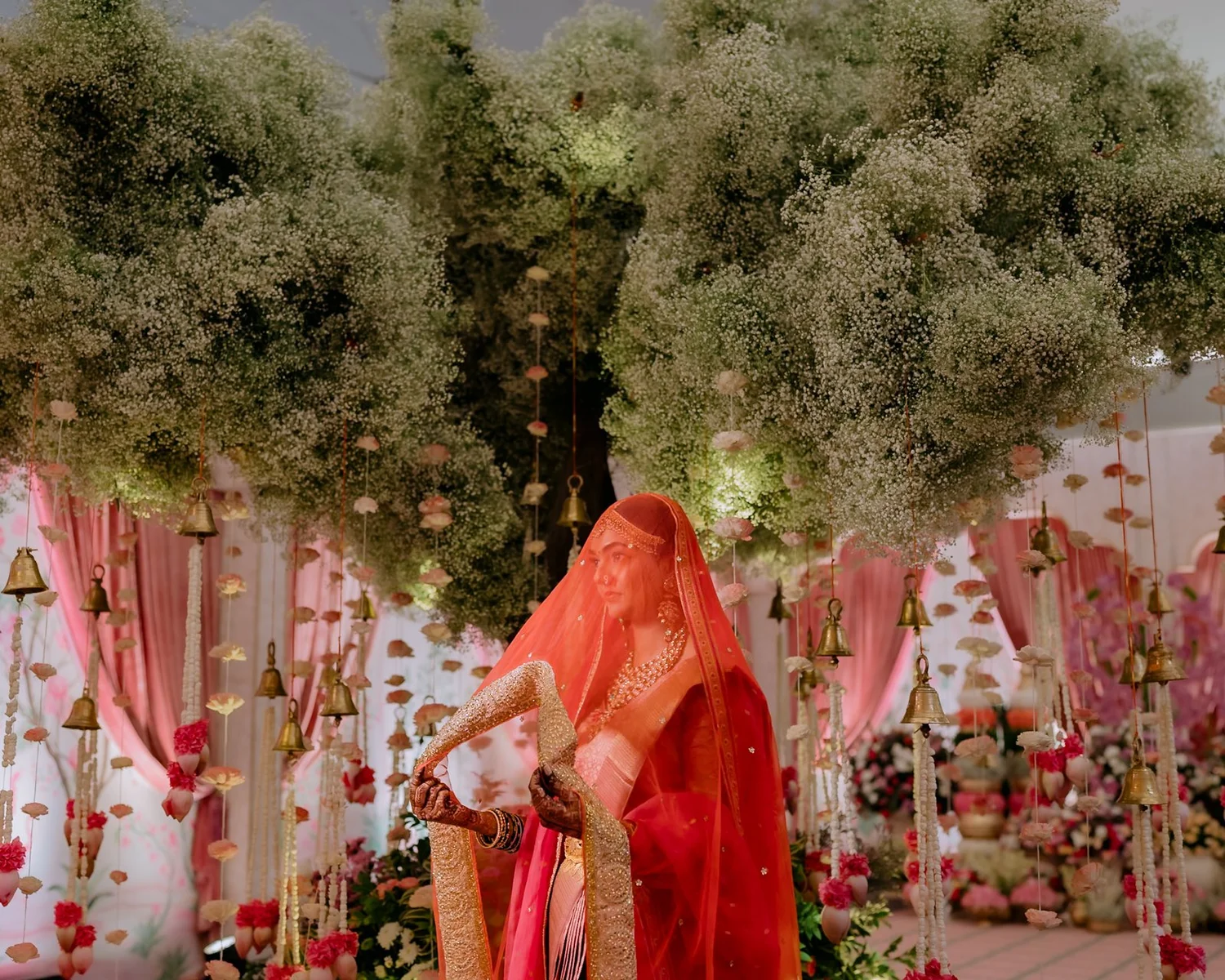 Shrishti in her red veil beneath the flowering trees