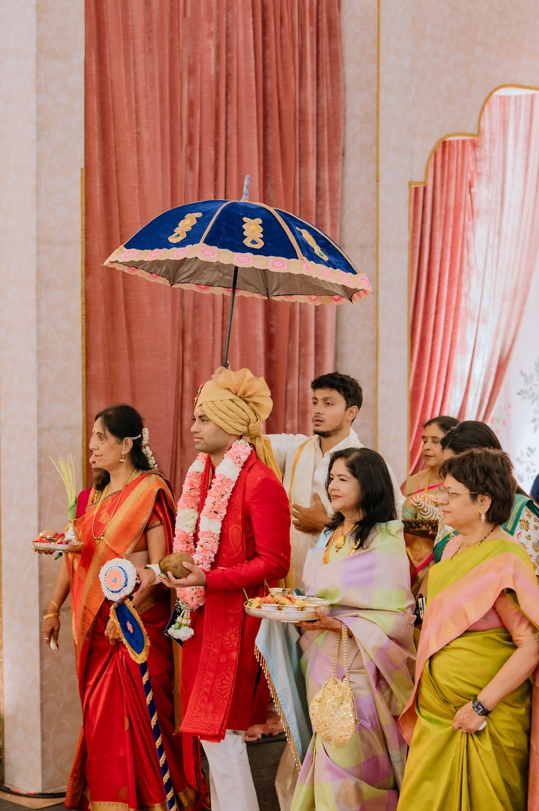 Akhil walking in under a blue ceremonial umbrella with his family