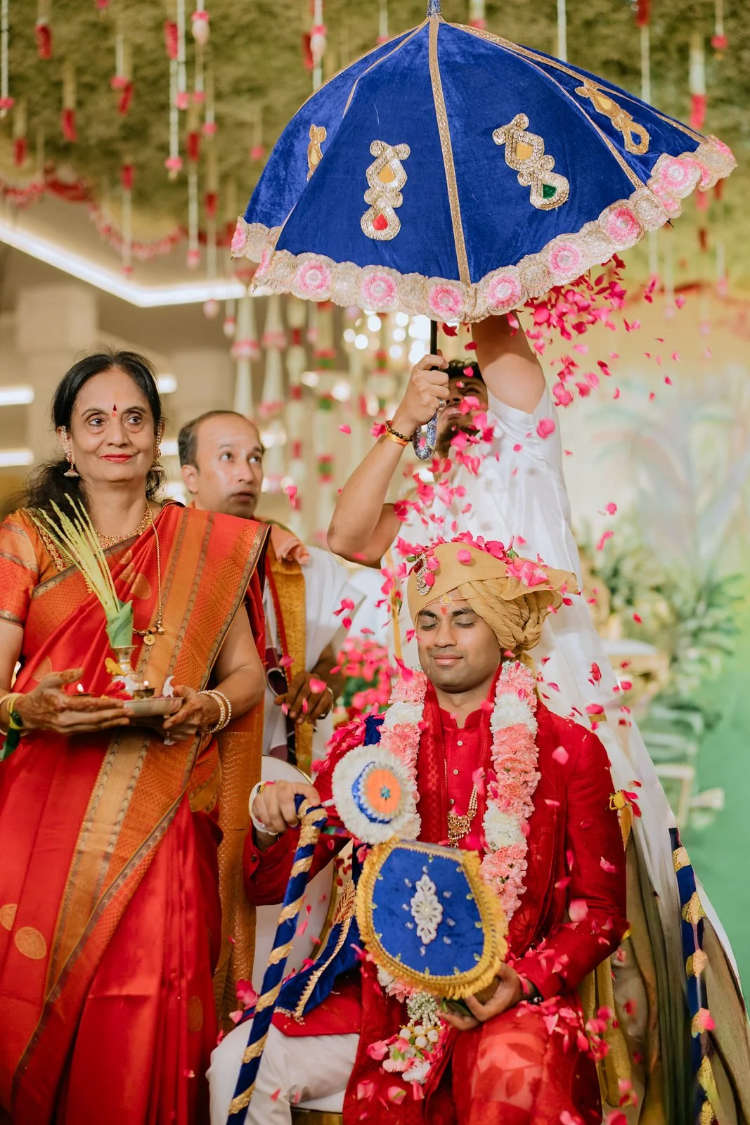 Akhil arriving under a blue ceremonial umbrella with family