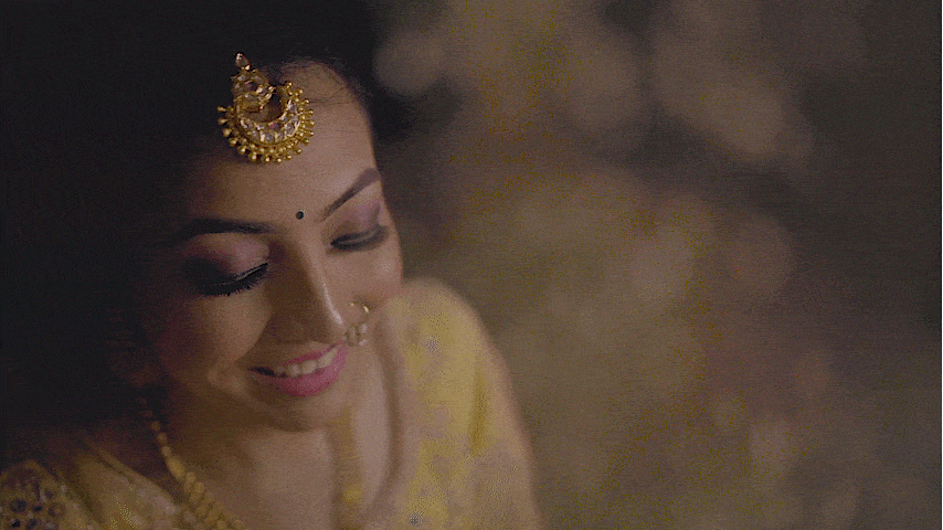 A woman wearing traditional Indian attire, including a gold headpiece, nose ring, and jewelry, smiling with her eyes closed.