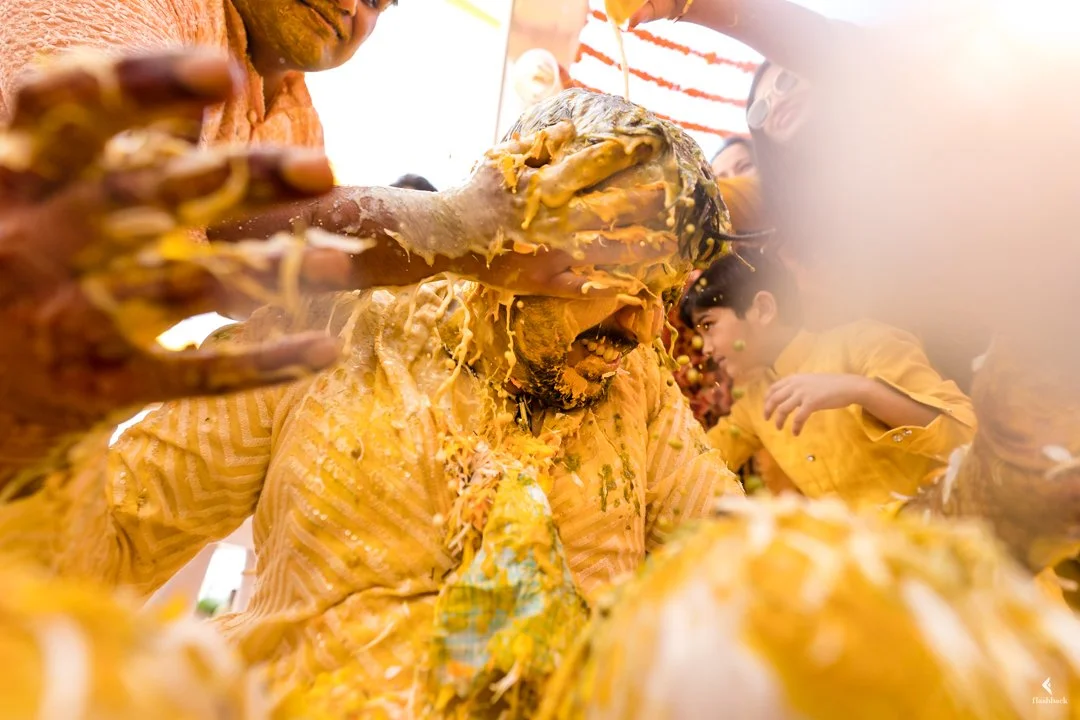 People covered in yellow and orange food, likely at a celebration or event, with one person being splattered with food while others enjoy the moment.