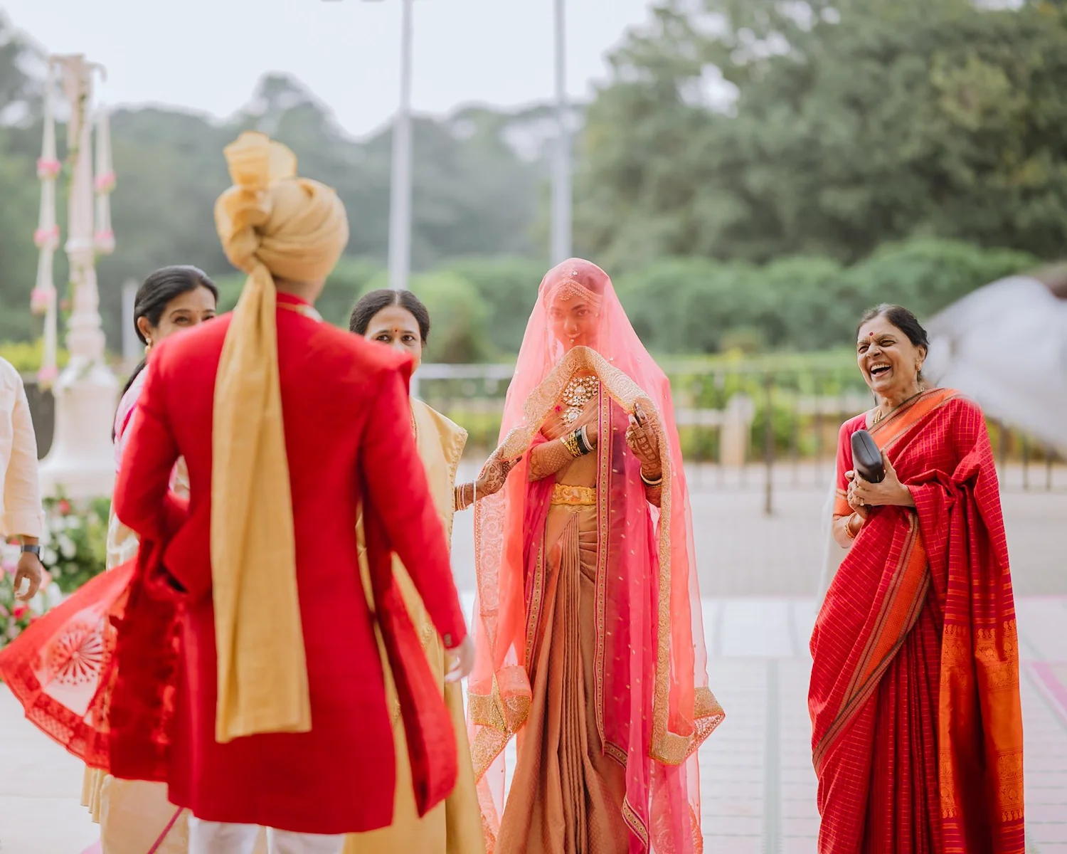 Akhil in a red bandhgala and gold safa meeting the veiled bride outdoors