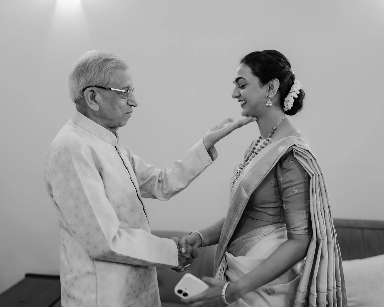 Shrishti's grandfather blessing her with a touch on the chin, black and white
