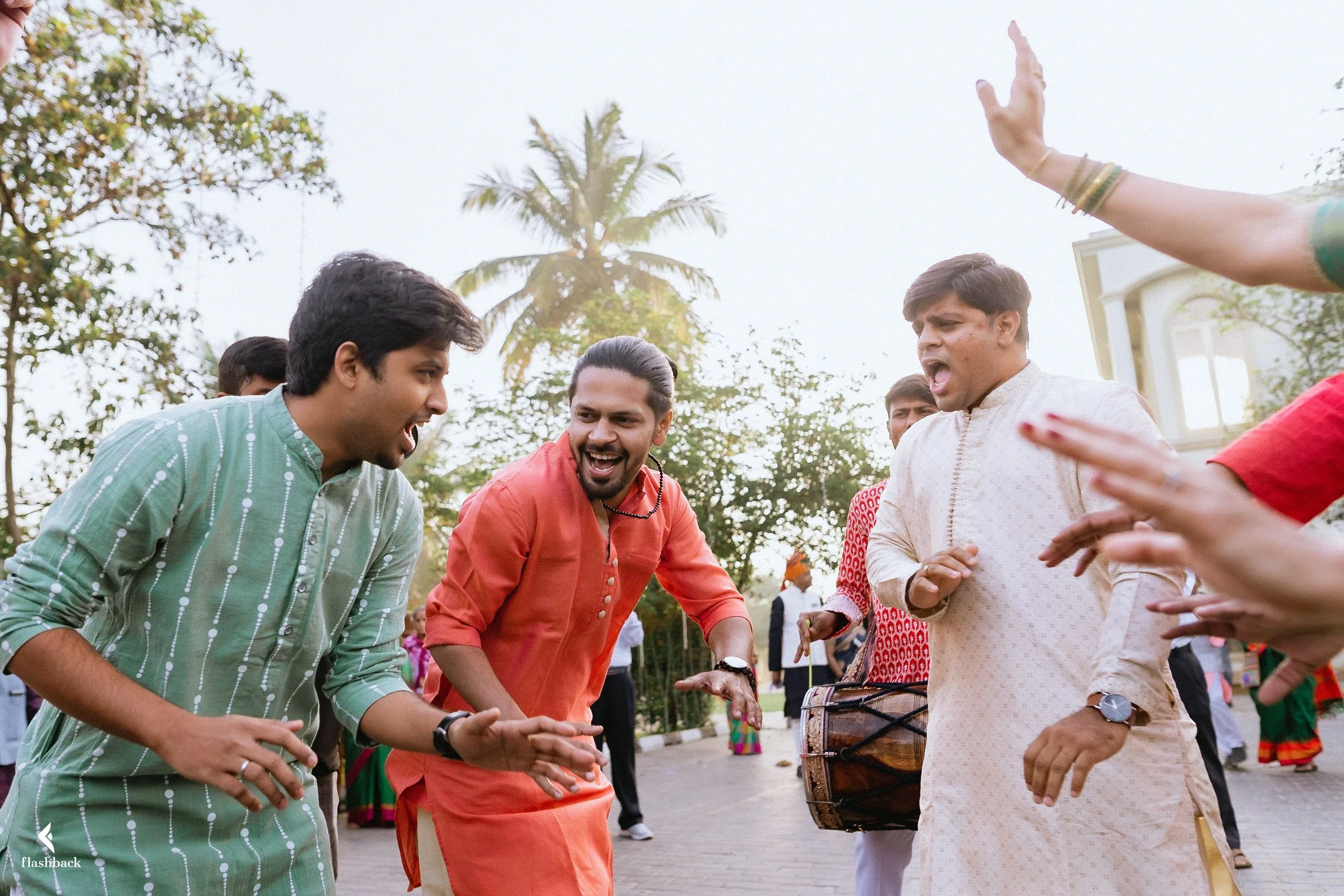 People celebrating and dancing outdoors, some playing drums, in traditional Indian attire.