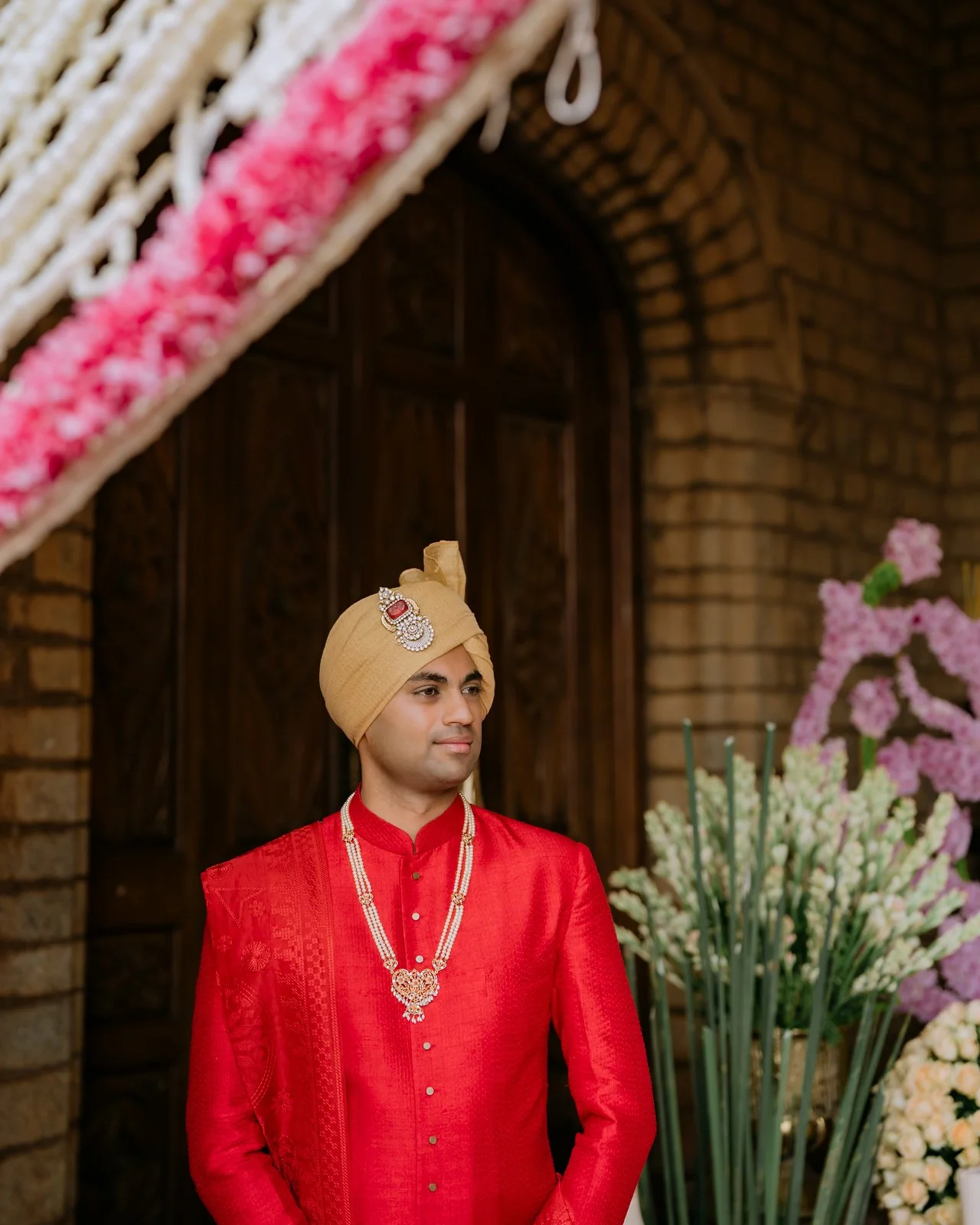 Akhil in a red sherwani and safa by a palace doorway