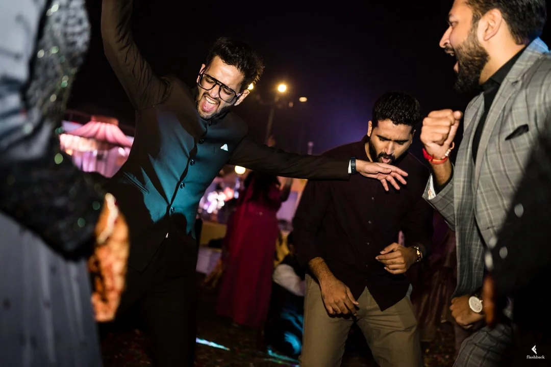Three men dancing and enjoying themselves at a party or celebration with colorful lighting.
