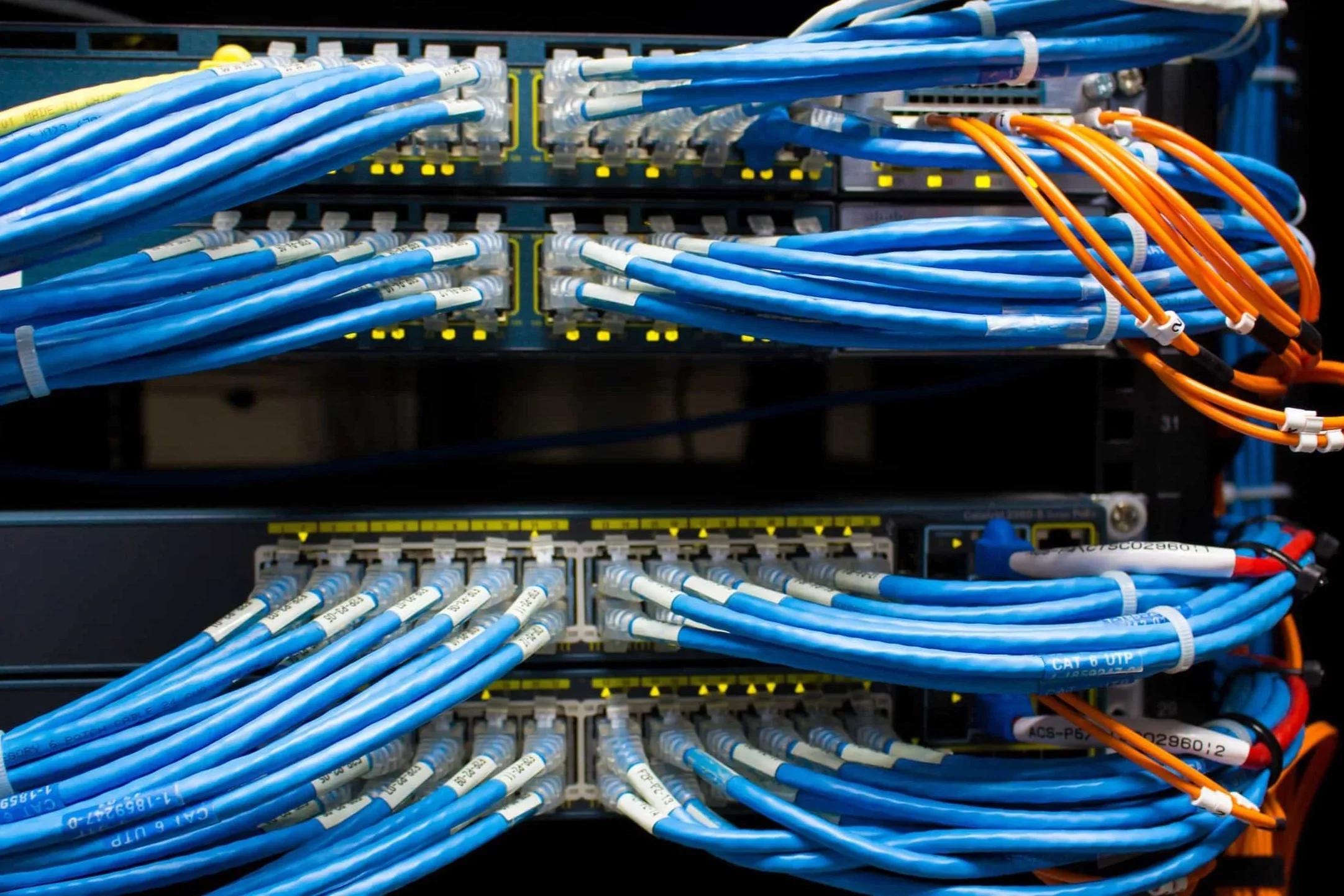 Network server rack with blue Ethernet cables connected to switches, with some orange cables on the side