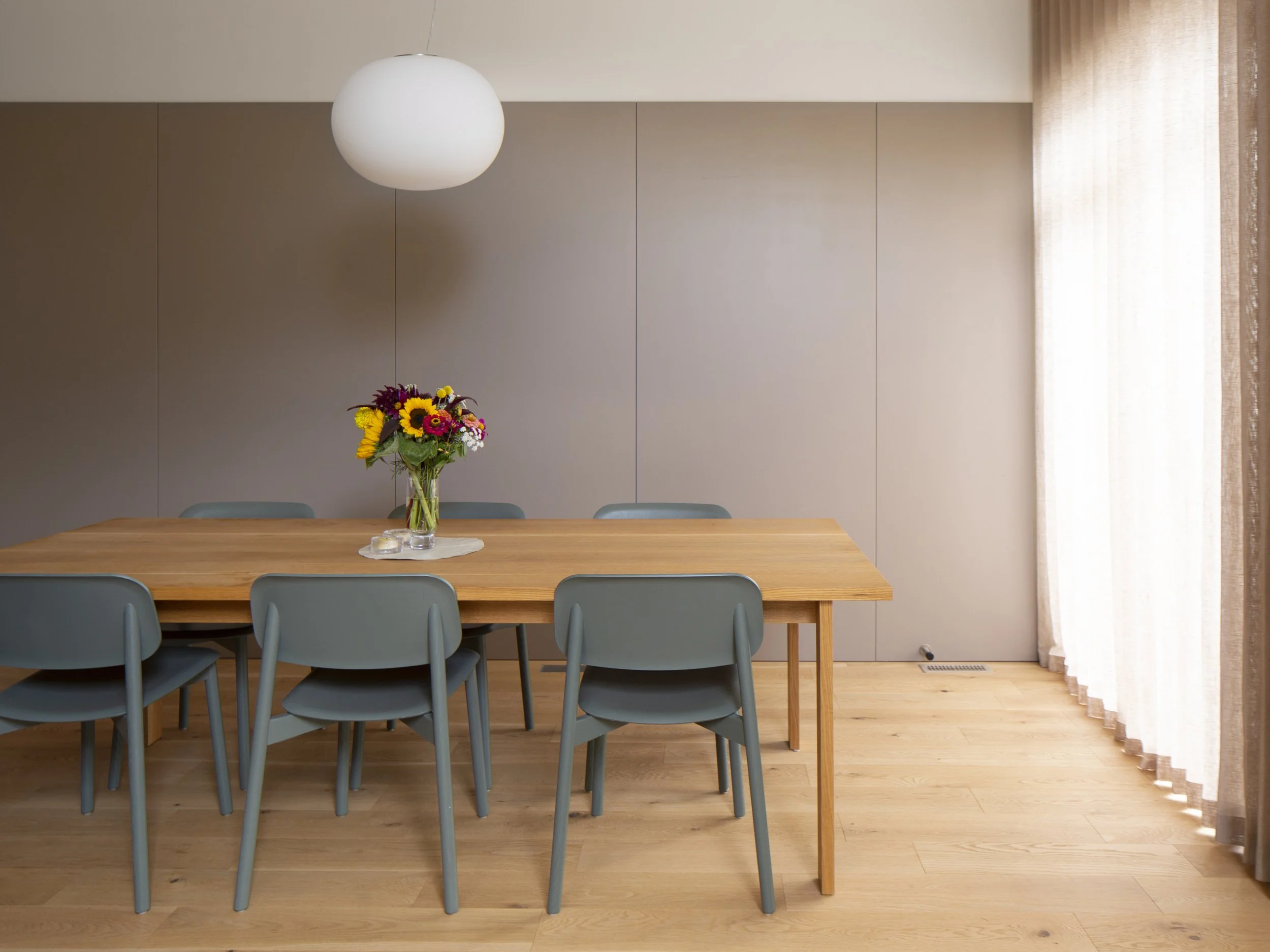Dining room of Bonnie Doon Duplex multi-family project in Bonnie Doon neighbourhood of Edmonton, Alberta, showing hardwood floor, wall paneling, linen drapes and custom oak table