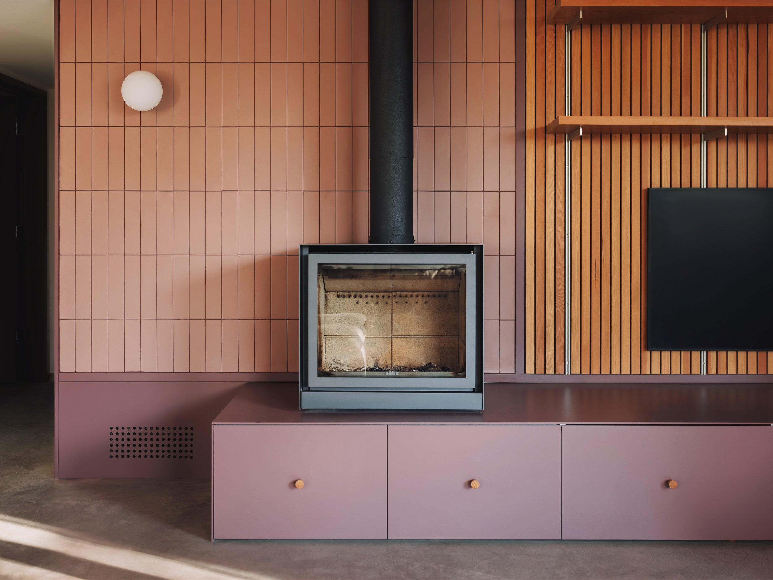 Fireplace with tiled surround and wood slat wall in living room of architectural cabin at Wabamun, Alberta near Edmonton