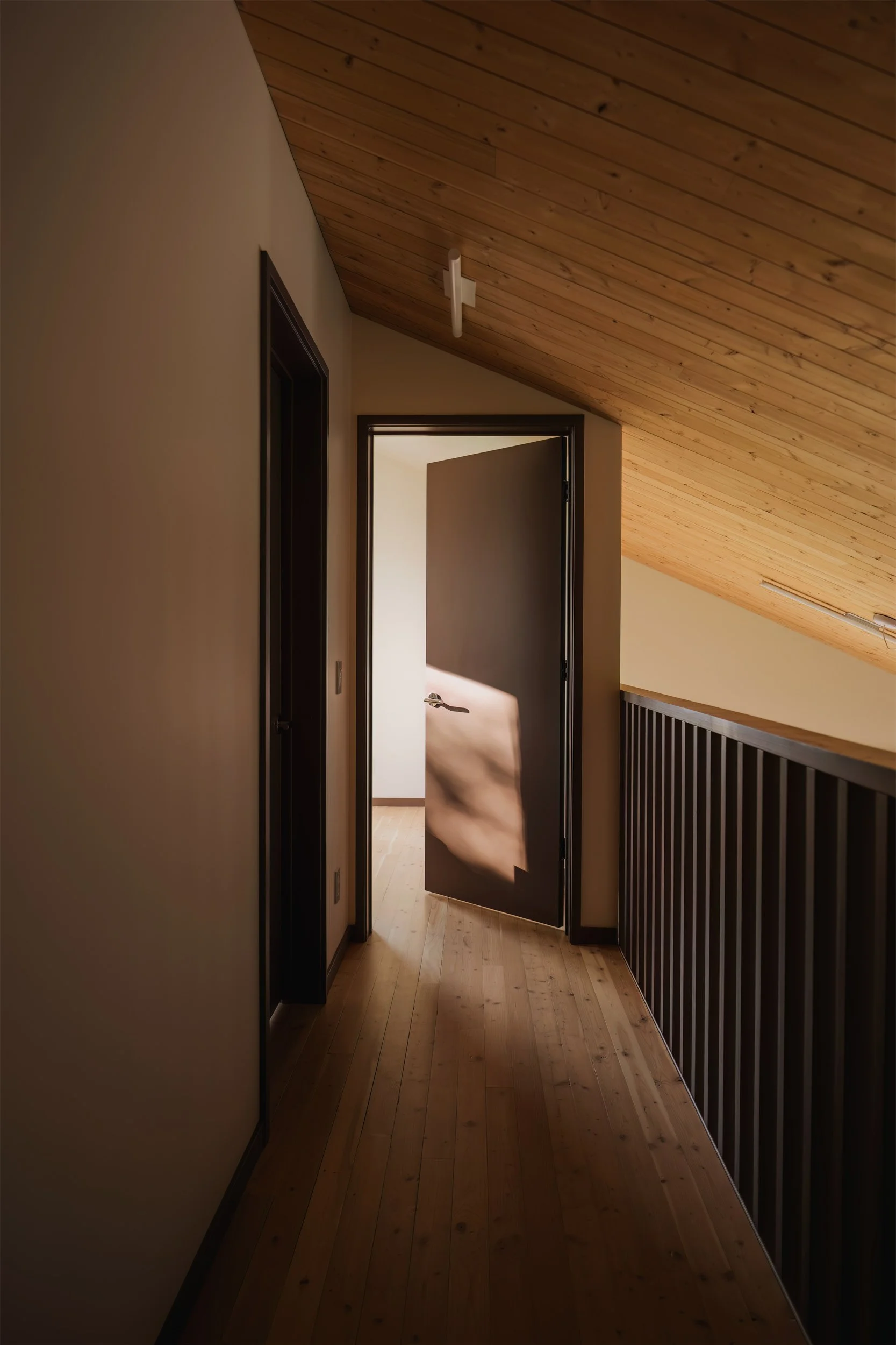 Door to primary bedroom of architectural cabin at Wabamun, Alberta near Edmonton showing custom railing, fir ceiling, double-height space