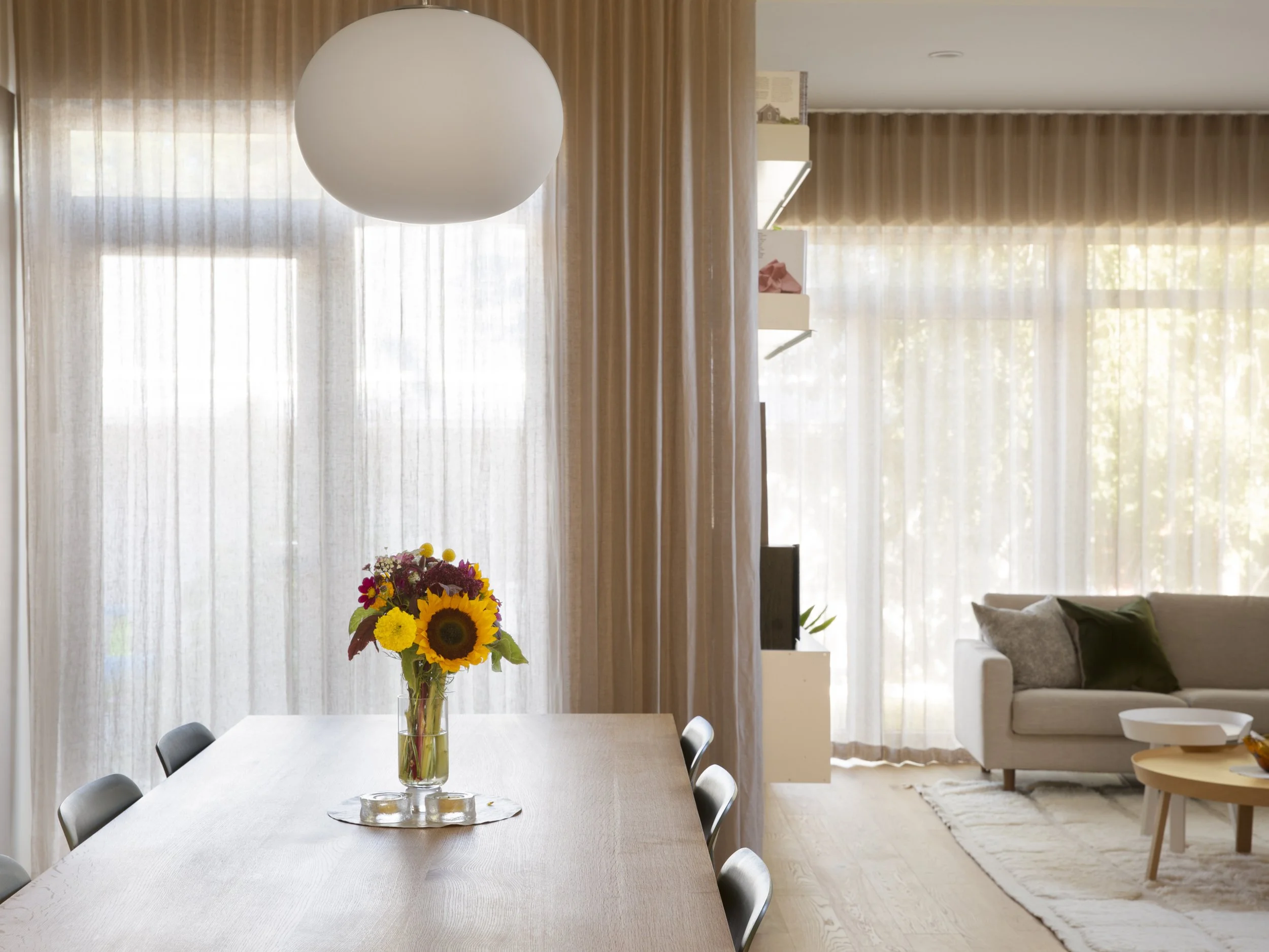 Dining room of Bonnie Doon Duplex multi-family project in Bonnie Doon neighbourhood of Edmonton, Alberta, showing linen drapes, shelving unit, and custom made oak table.