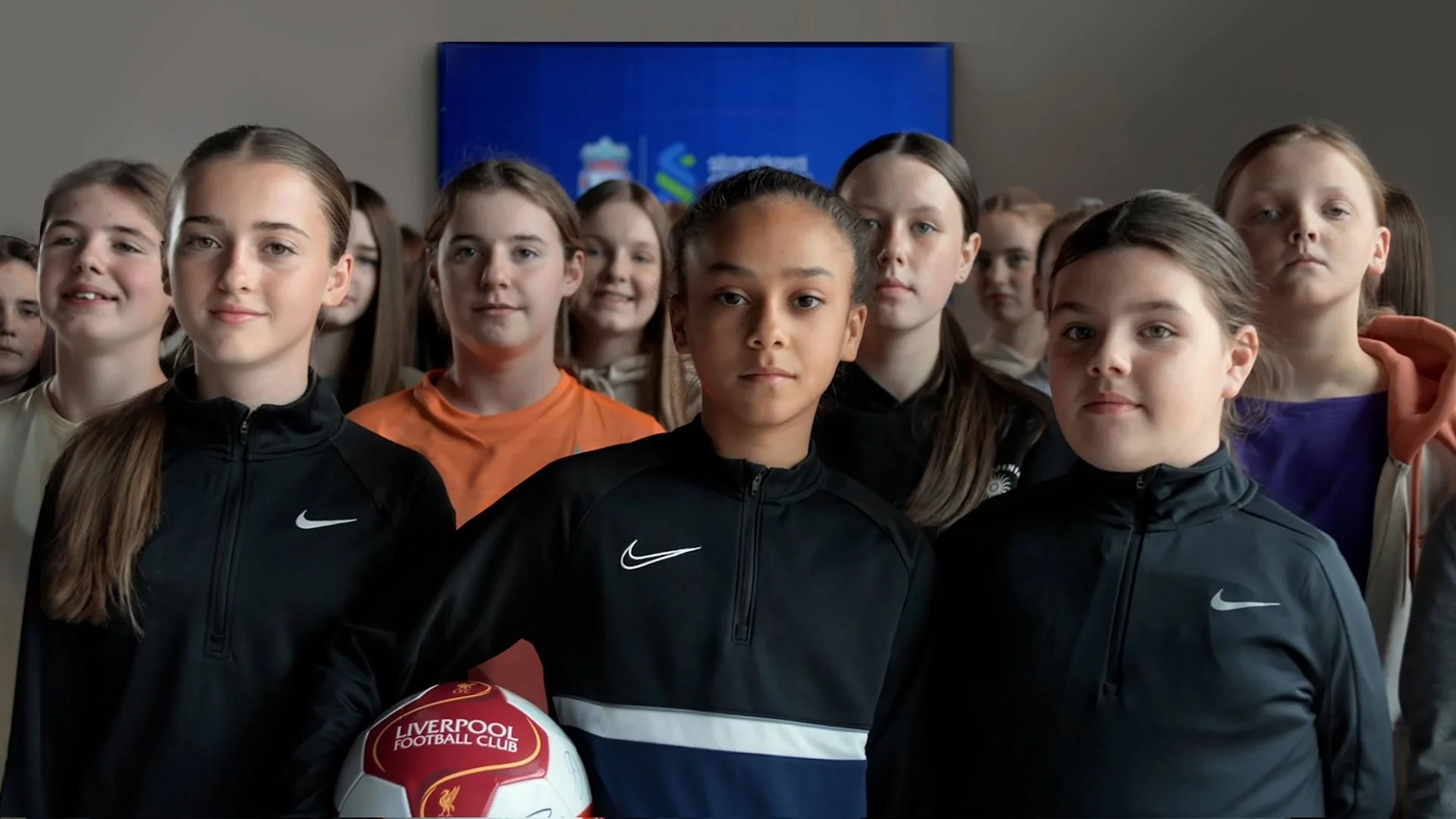 A group of girls aged between 12 and 16 holding onto a football with a look of dedication on their face
