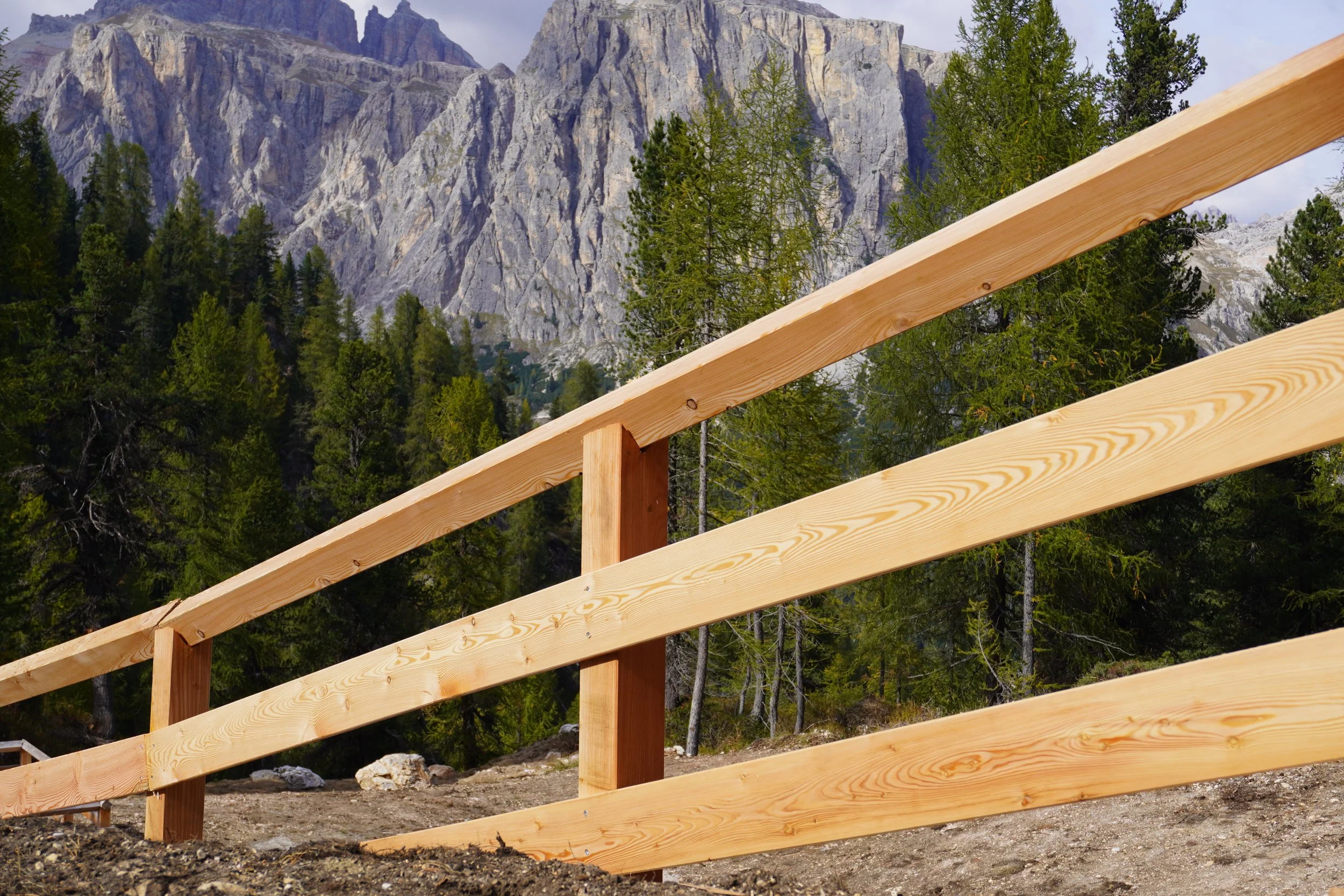 Travi di legno non finite, con uno sfondo di montagne rocciose e alberi di conifere.