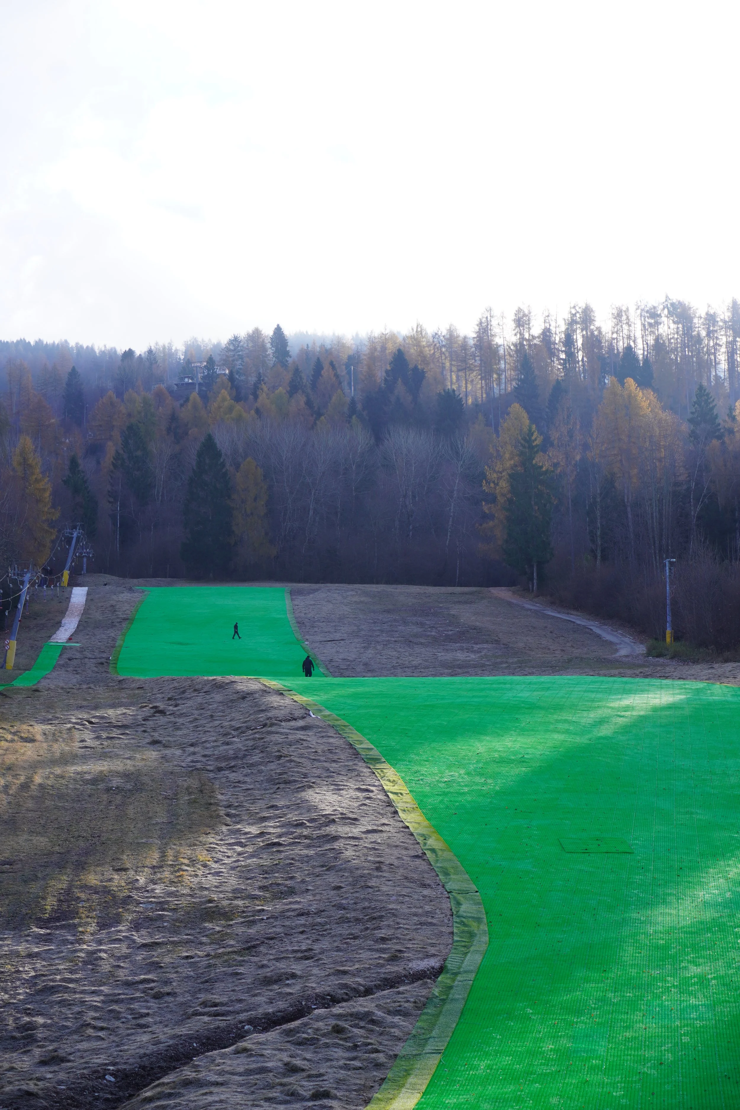 Impianti di sci in costruzione con percorsi verdi e alberi in lontananza.