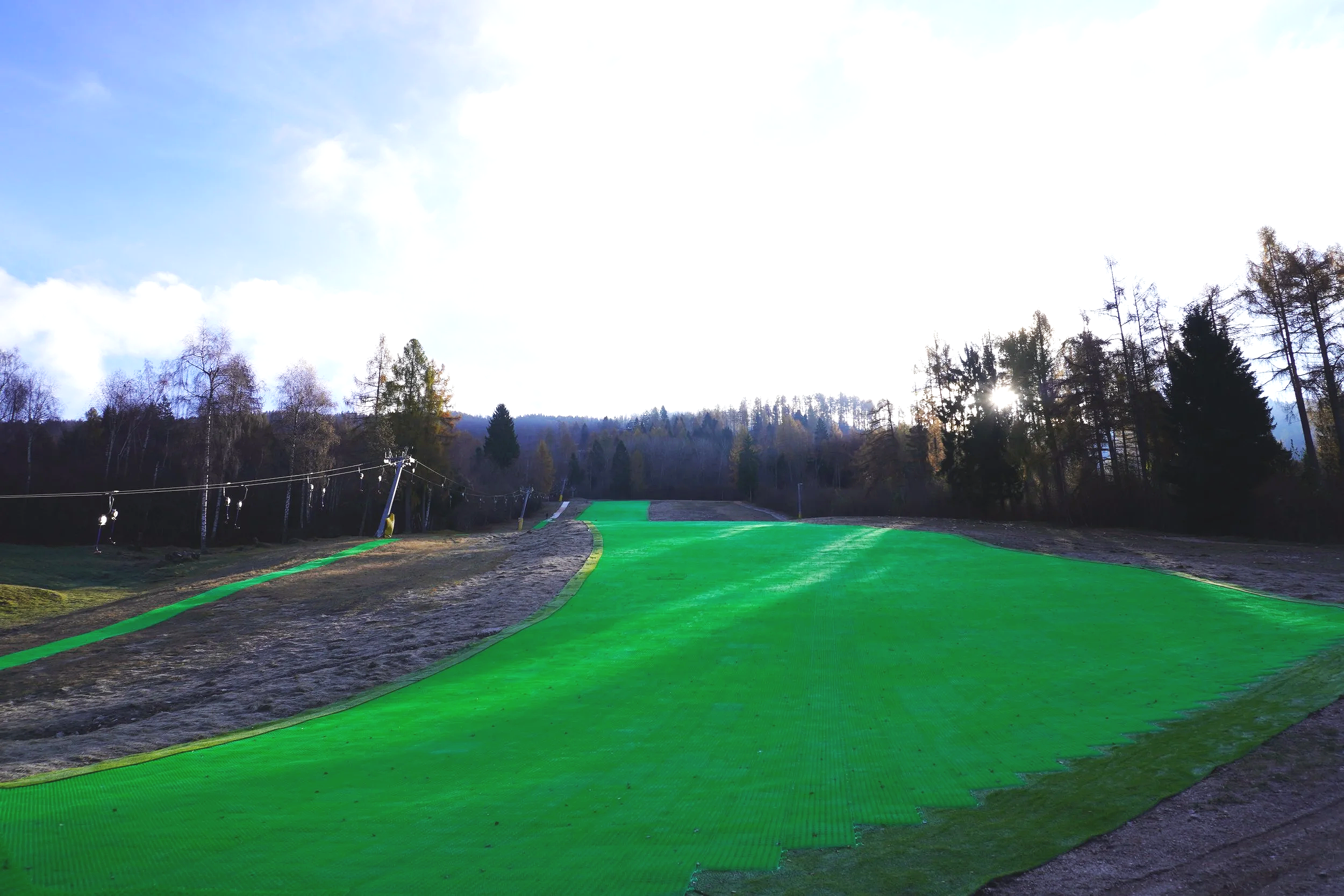 Pista da sci artificiale in fase di costruzione con terreno e alberi sullo sfondo