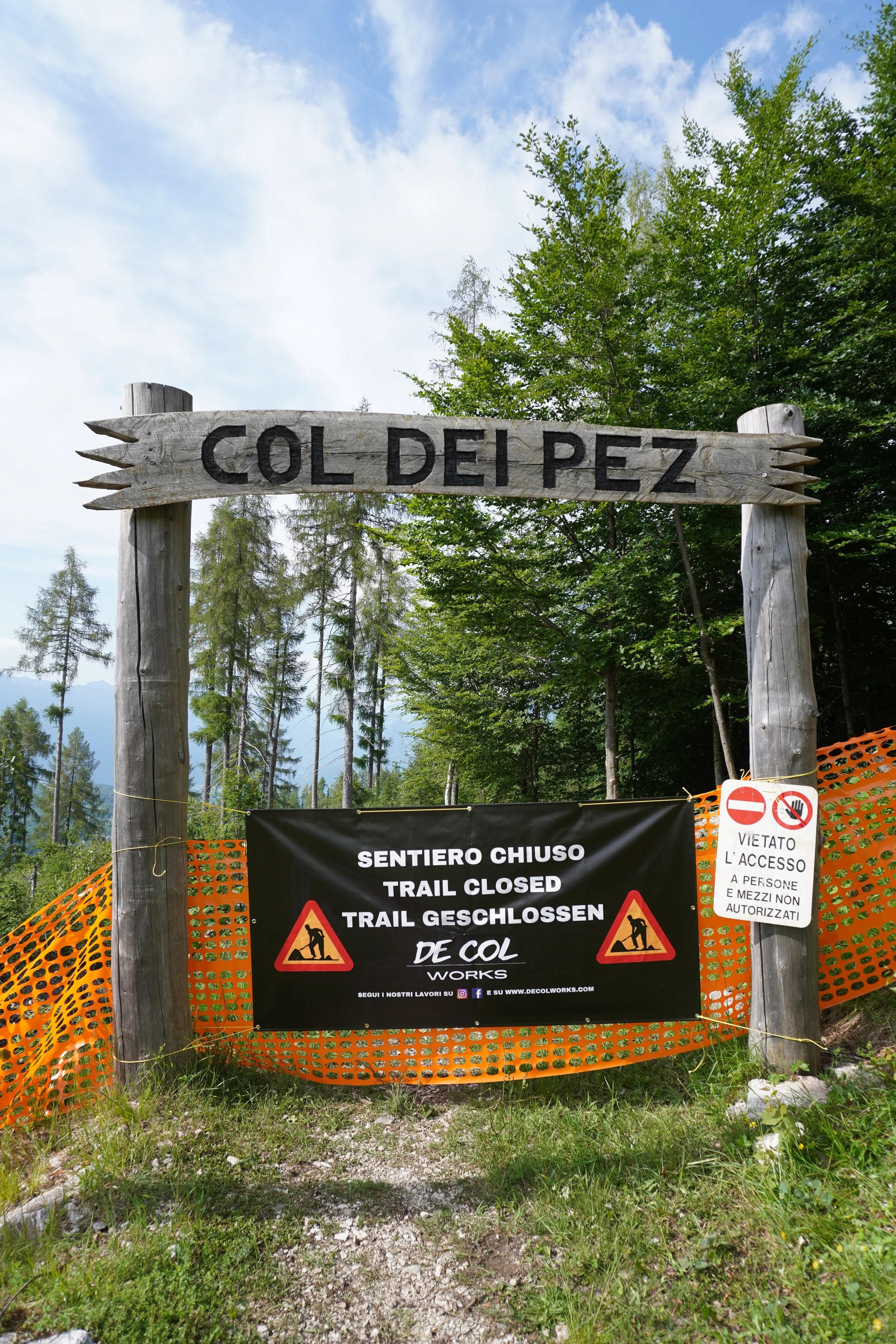 Cartello di un sentiero chiuso con avviso di lavori di restauro, in un'area boschiva con alberi e cielo nuvoloso.