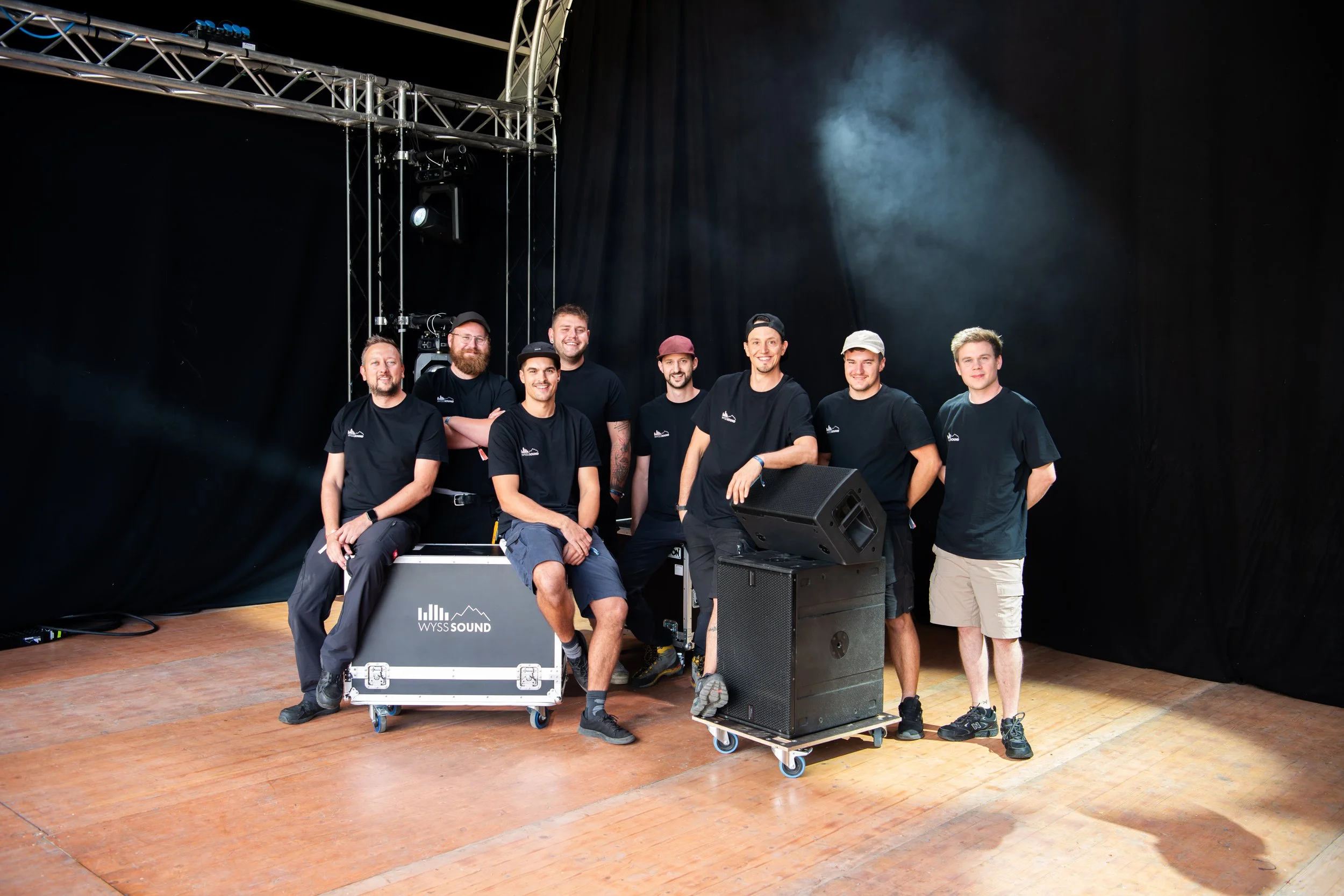 Sieben Männer stehen hinter Ton- und Lichttechnik auf einer Bühne.