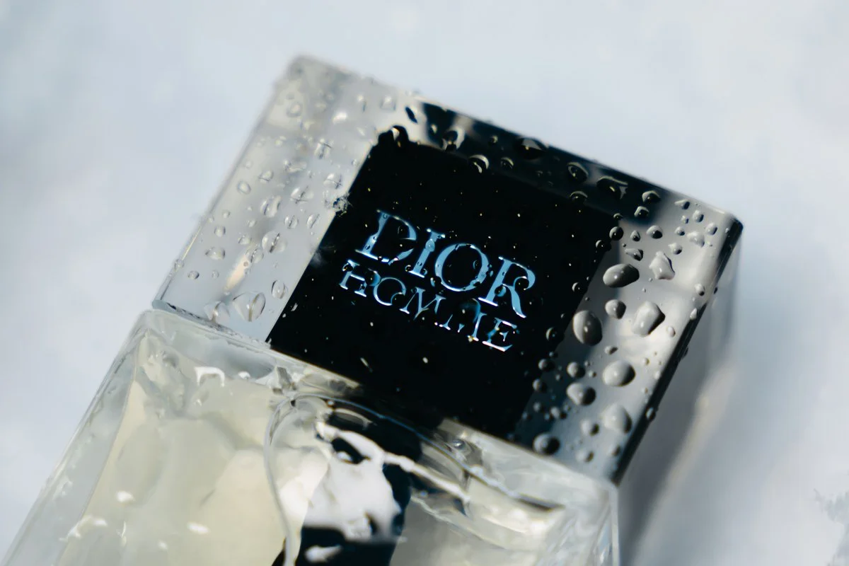 Photographie de produit luxe par Mélissa Pottier. Flacon de parfum Dior Homme sur surface mouillée, jeu de reflets et de matières pour un rendu premium.