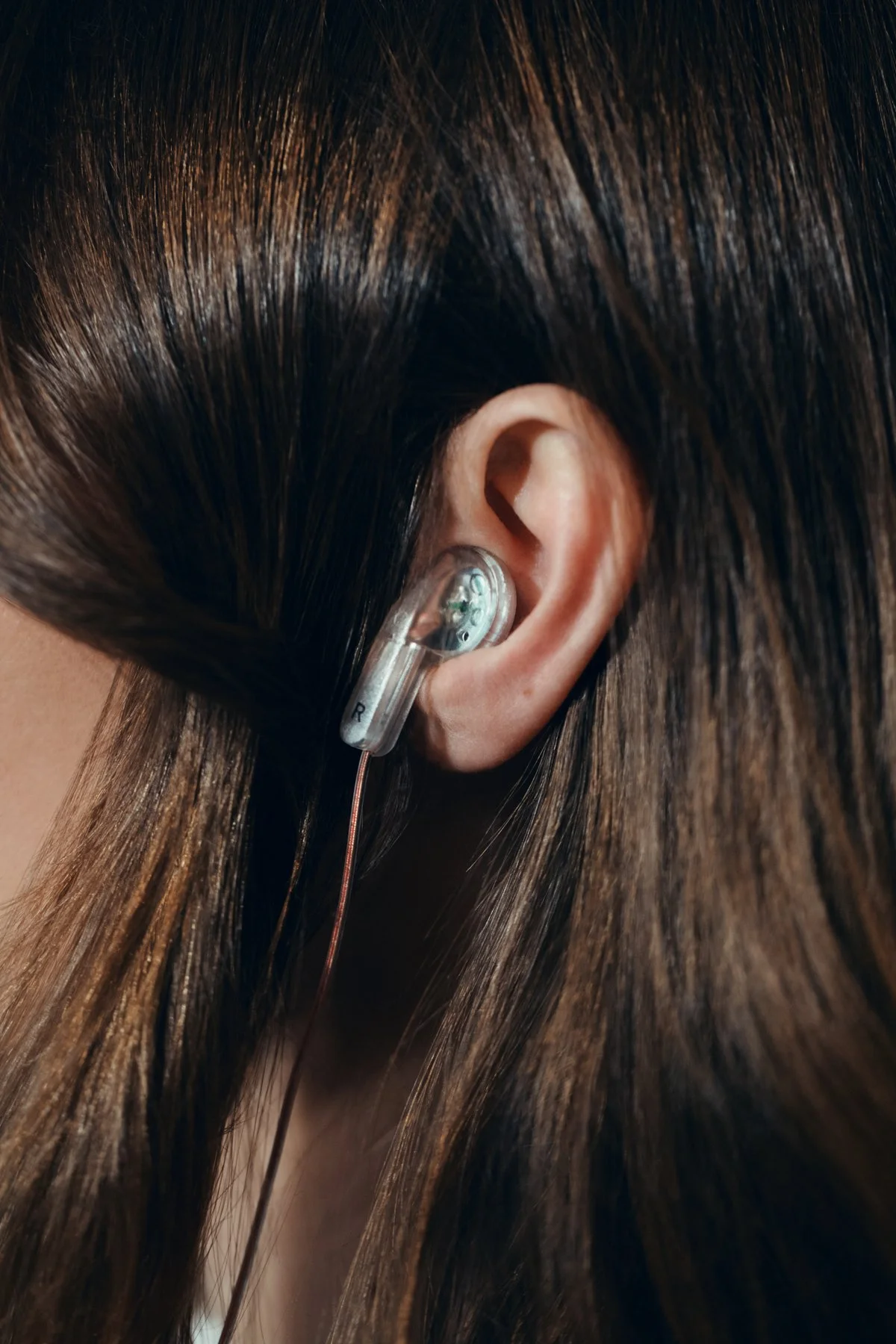 Photographie produit tech et lifestyle par Mélissa Pottier. Gros plan sur une oreille portant un écouteur transparent, mise en scène minimaliste pour une campagne audio.