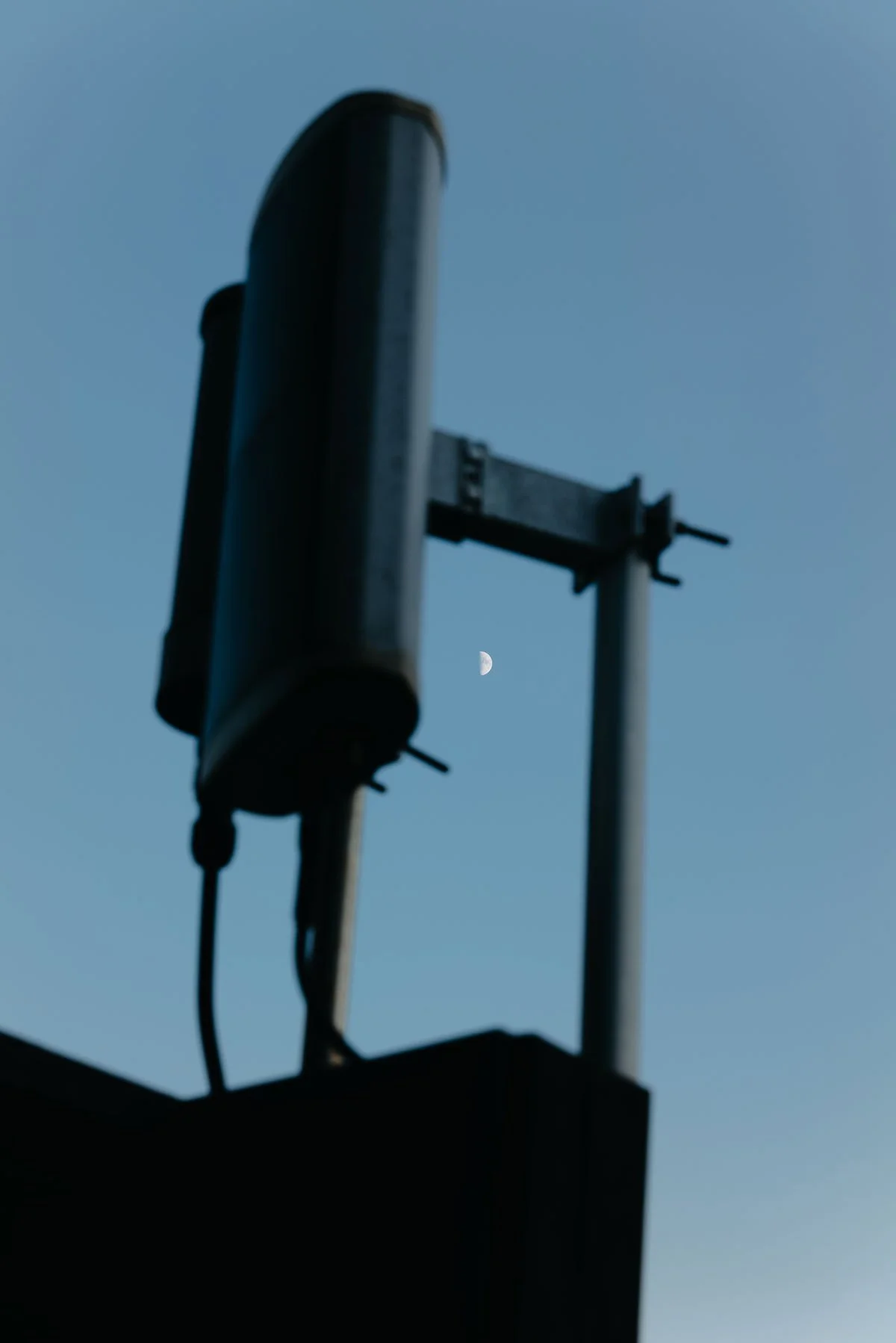Photographie architecturale et urbaine par Mélissa Pottier. Silhouette d'une structure industrielle se découpant sur un ciel bleu, la lune apparaît, pour un éditorial graphique.
