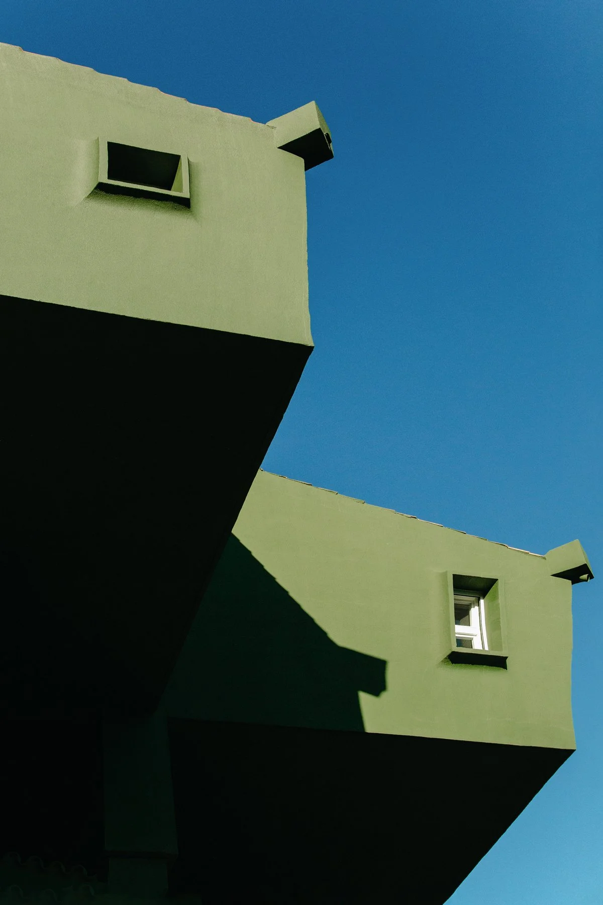 Photographie architecturale et urbaine par Mélissa Pottier. Angle d'un bâtiment aux teintes vertes se découpant sur un ciel bleu vif, composition graphique et contemporaine.