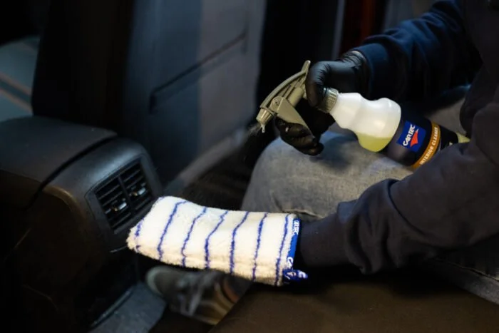 Persoon met gloved hands reinigt een auto vent uit met een sprayflacon.
