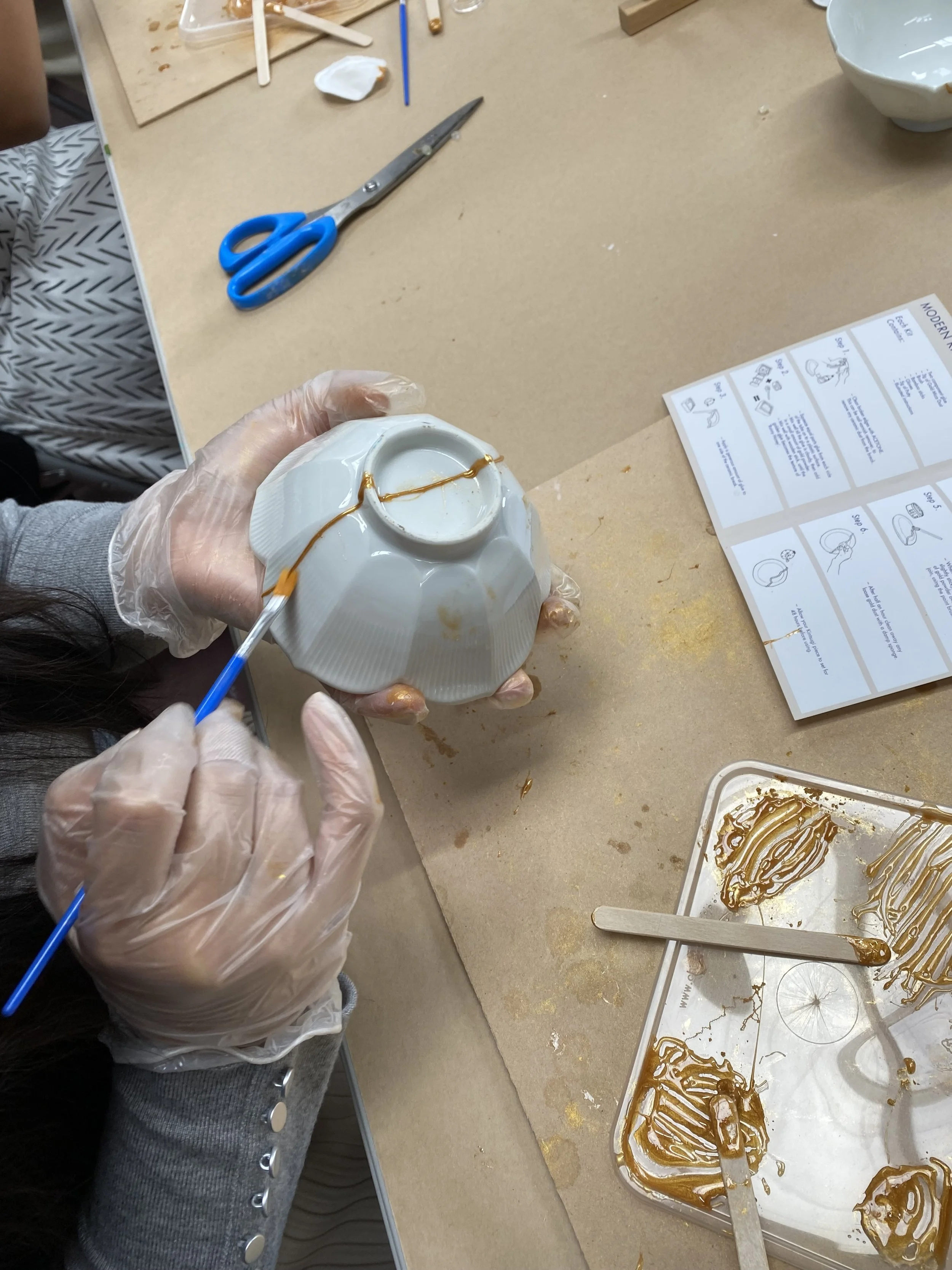 Person wearing plastic gloves piping caramel into a mold for candy or chocolates on a worktable with tools, instructions, and caramel syrup.