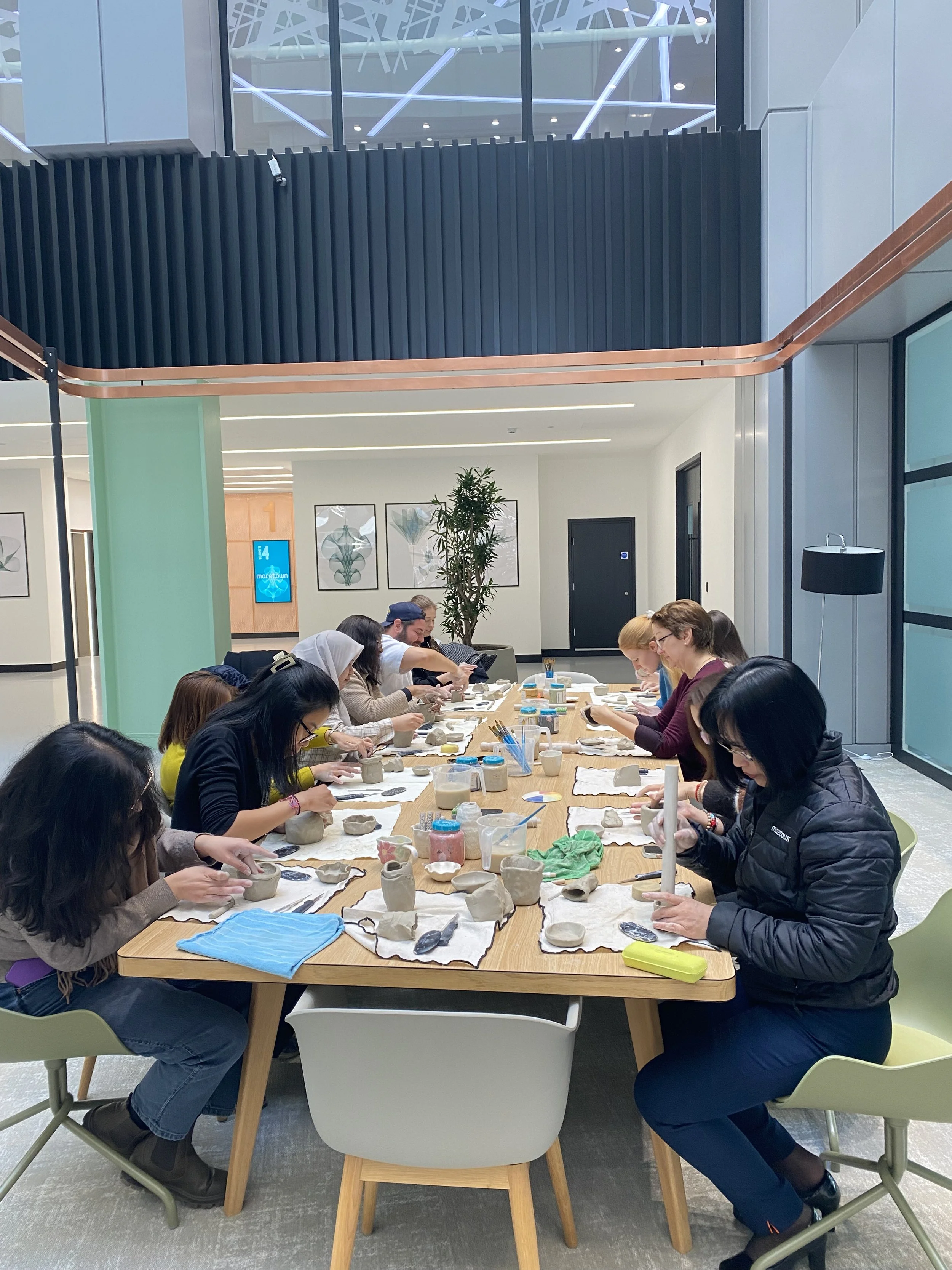 Group of diverse people sitting at a long table participating in a pottery workshop, working on clay pottery projects.